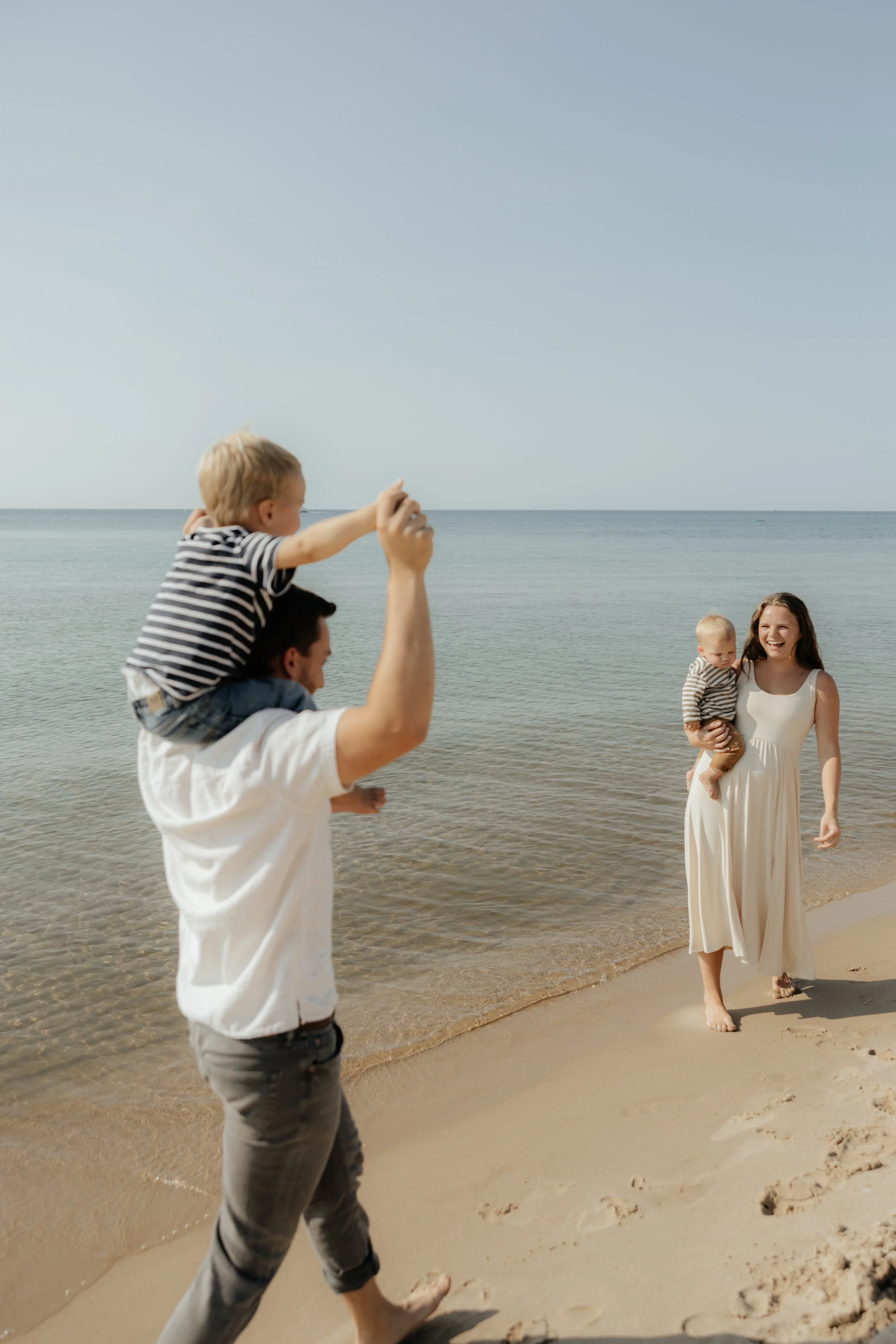 A happy family enjoying a day at the beach in Michigan, with candid and easy posing, all smiling and walking along the shoreline with Lake Michigan in the background.