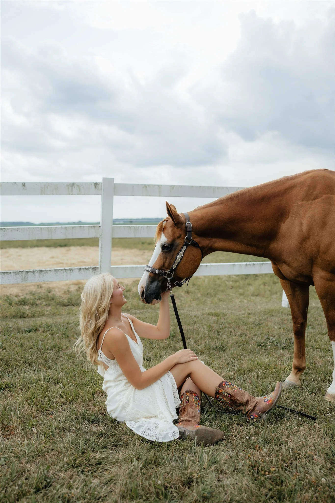 A high school senior posing with her horse for personal senior photos in West Michigan on farm with white fence and grassy area.