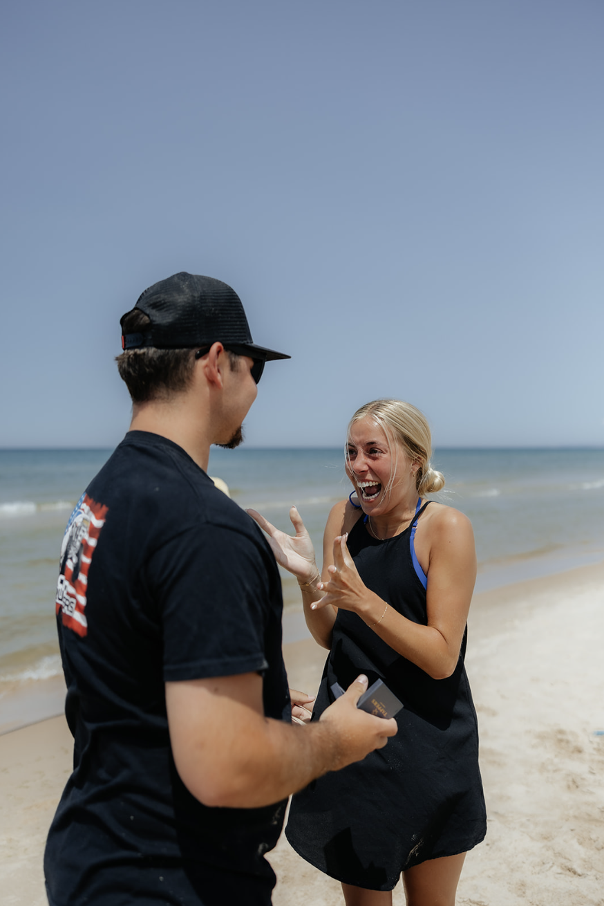 Surprise proposal at beach at Silver Lake Sand Dunes, summer wedding planning, documentary moment.