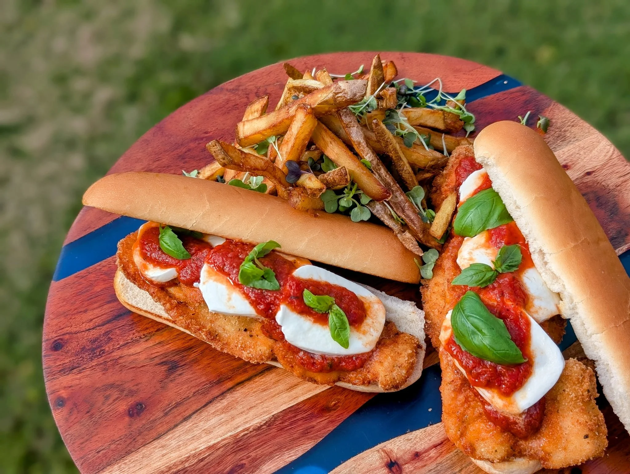 Two fish sandwich sliders with basil leaves, served with French fries and microgreens on a wooden serving board