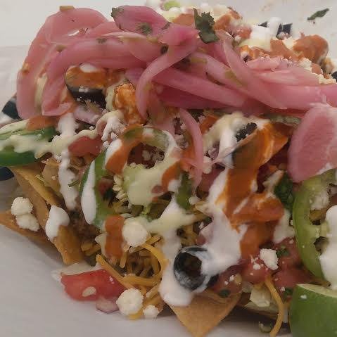 A plate of nachos topped with diced tomatoes, shredded cheese, sour cream, pickled red onions, jalapeños, black beans, and chopped herbs.