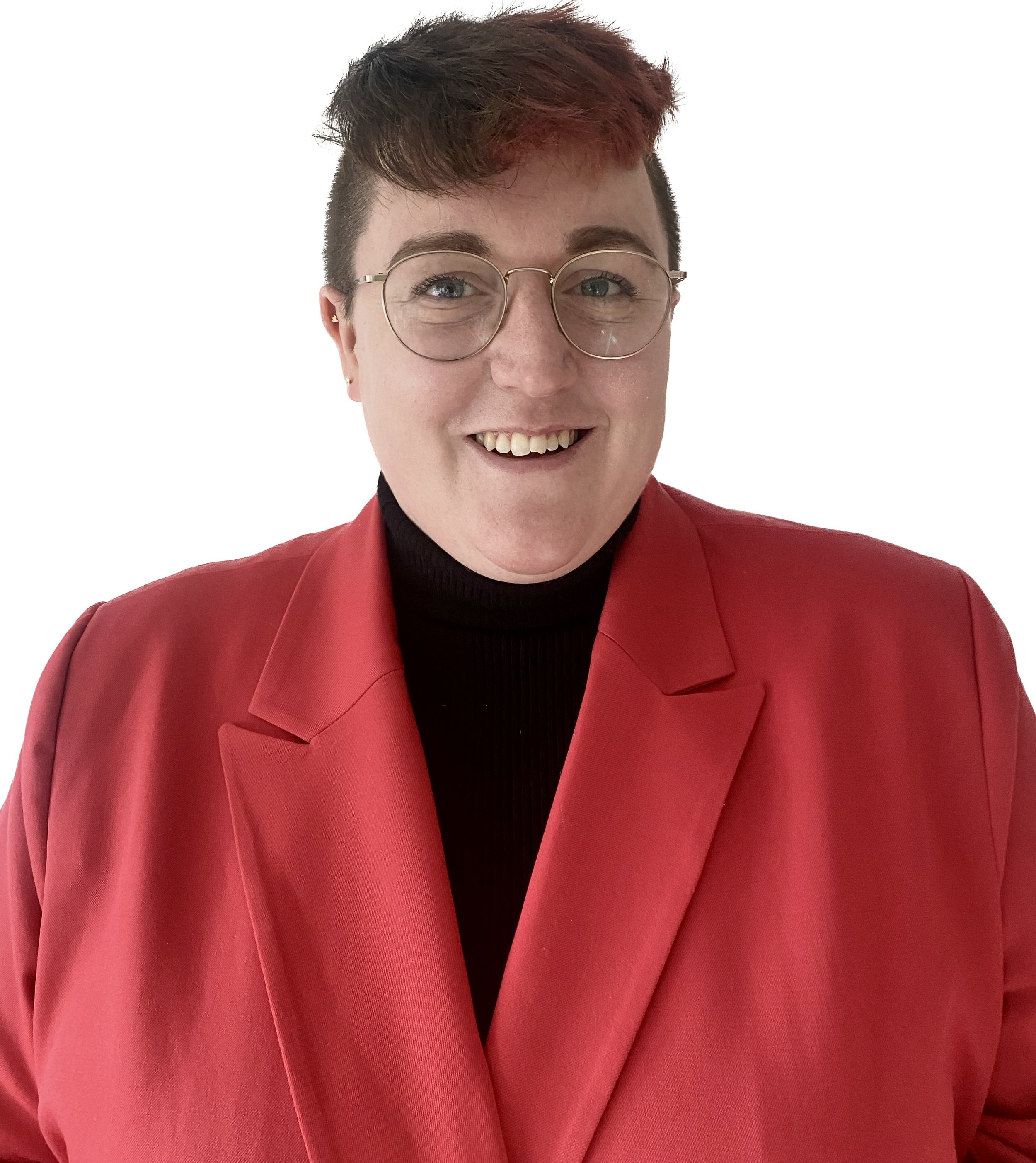 A person wearing a red blazer over a black turtleneck jumper and glasses smiles at the camera. The side of their head is shaved and they have brown hair with a red highlight on top
