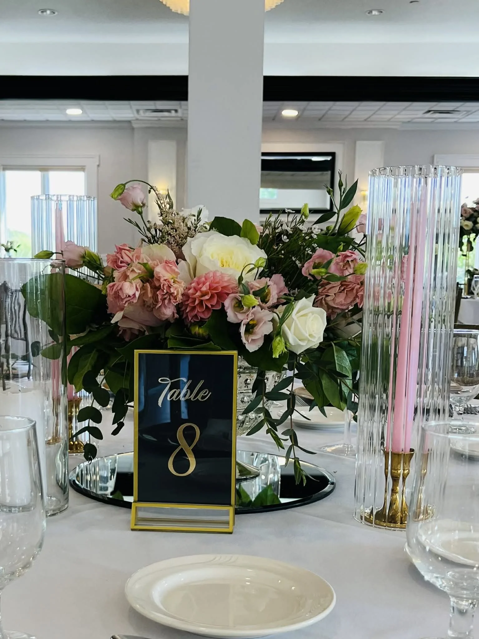 Elegant table centerpiece with pink and white flowers, glass candle holders, and a table sign indicating "Table 8" at a formal event.