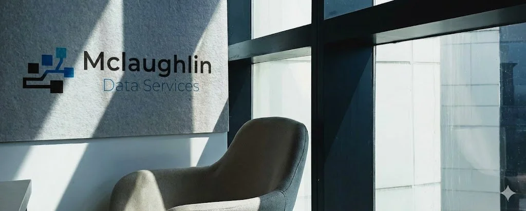 Interior of an office with a gray armchair, light coming through large windows, and a sign that reads 'McLaughlin Data Services' on the wall.