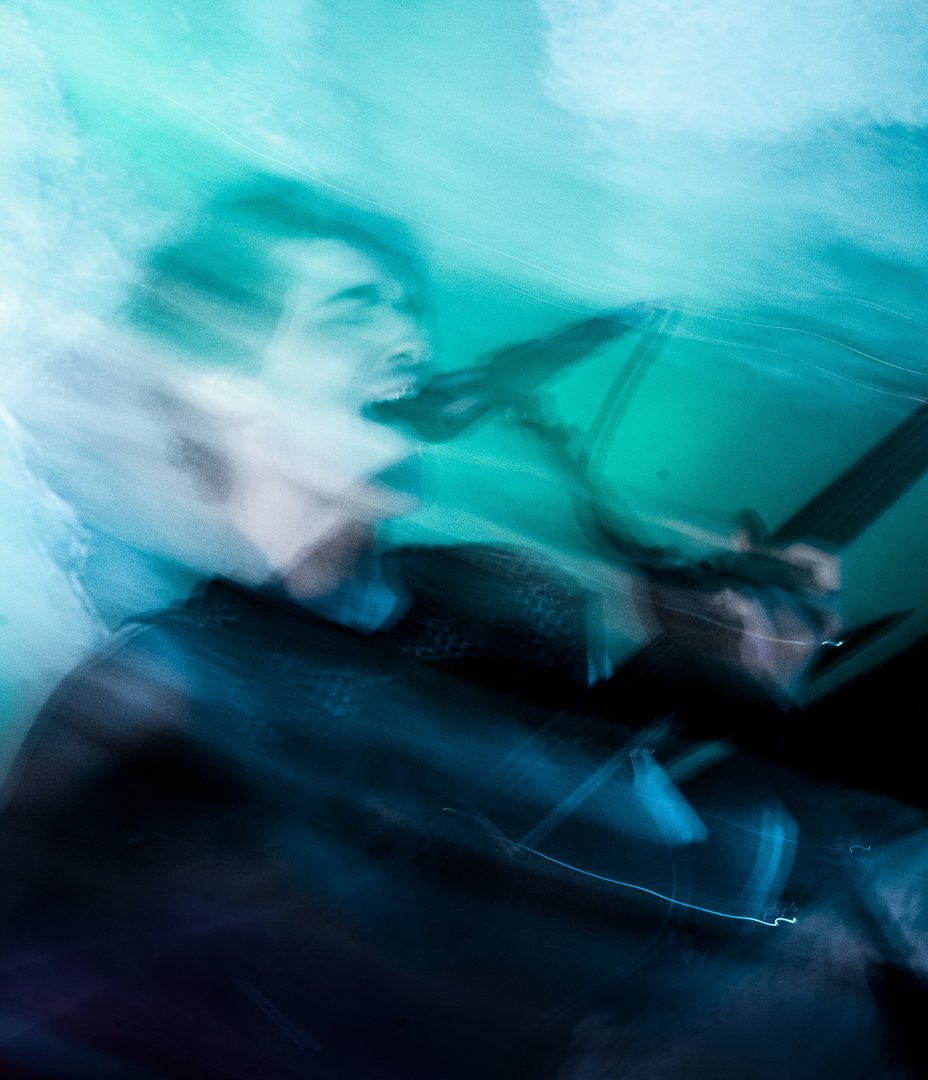 A person singing into a microphone in a blurred, abstract photo with shades of blue and teal.