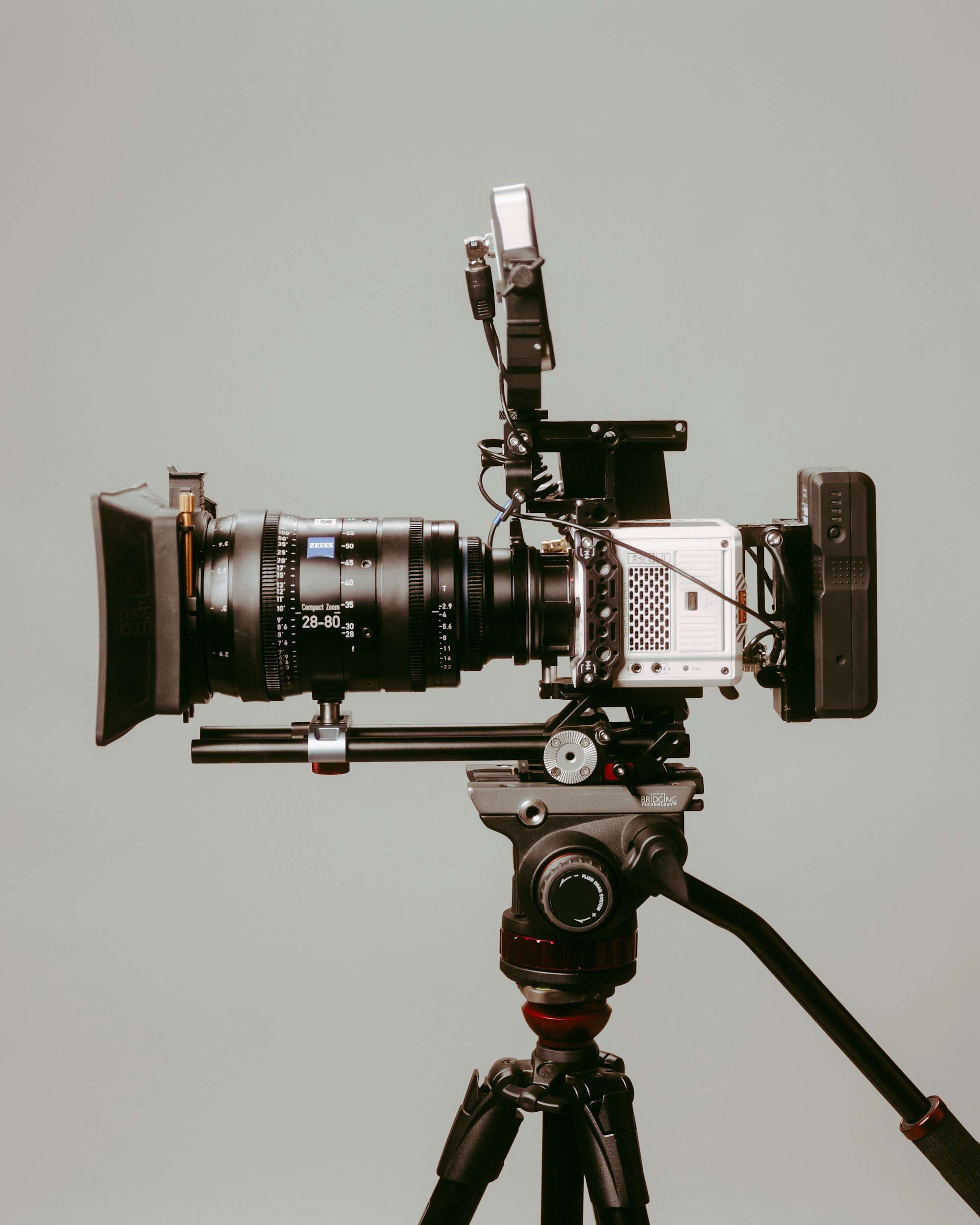Camera mounted on a tripod with various accessories in front of a plain background.