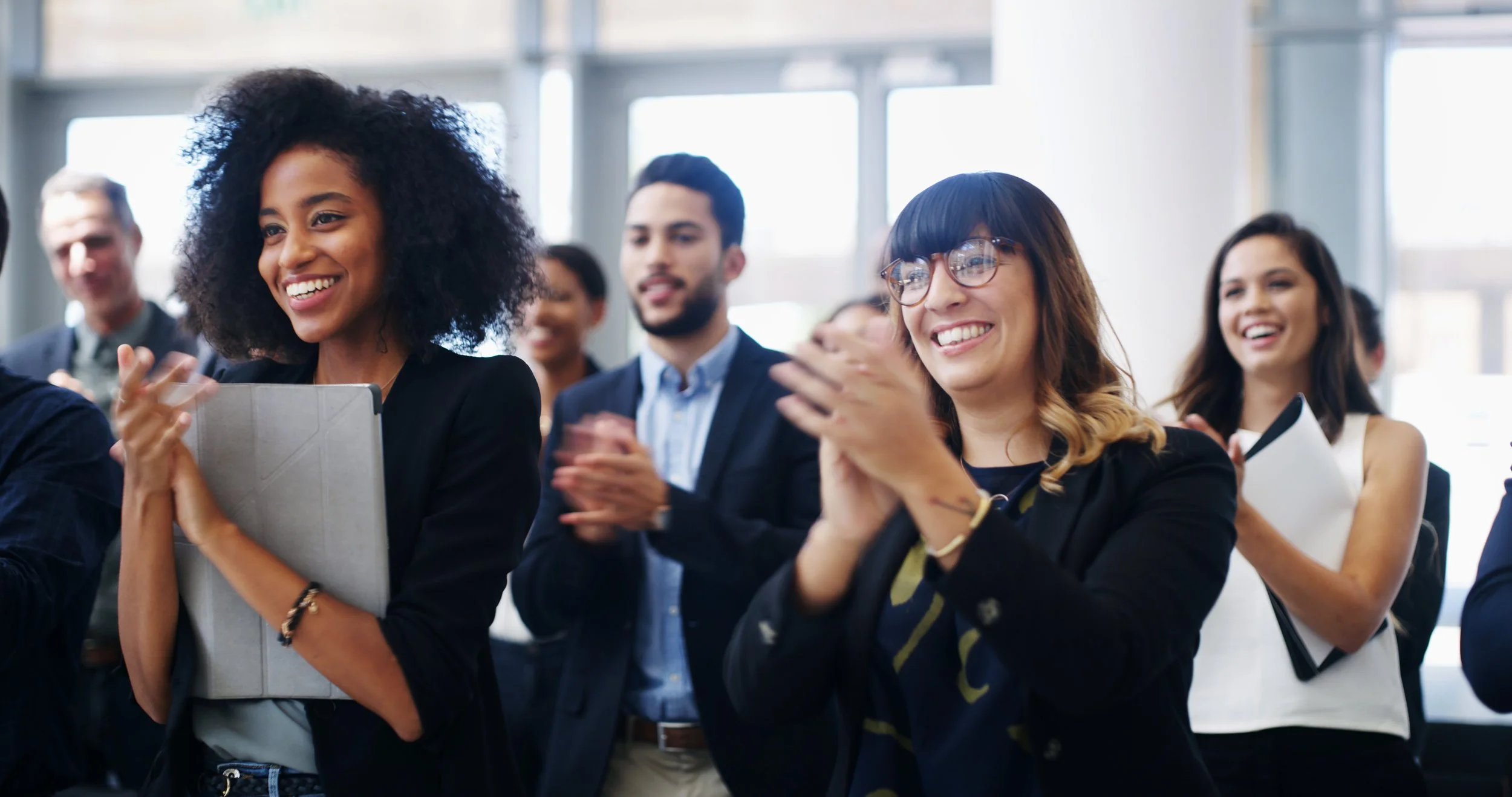 Group of diverse business professionals at a conference, smiling and clapping.