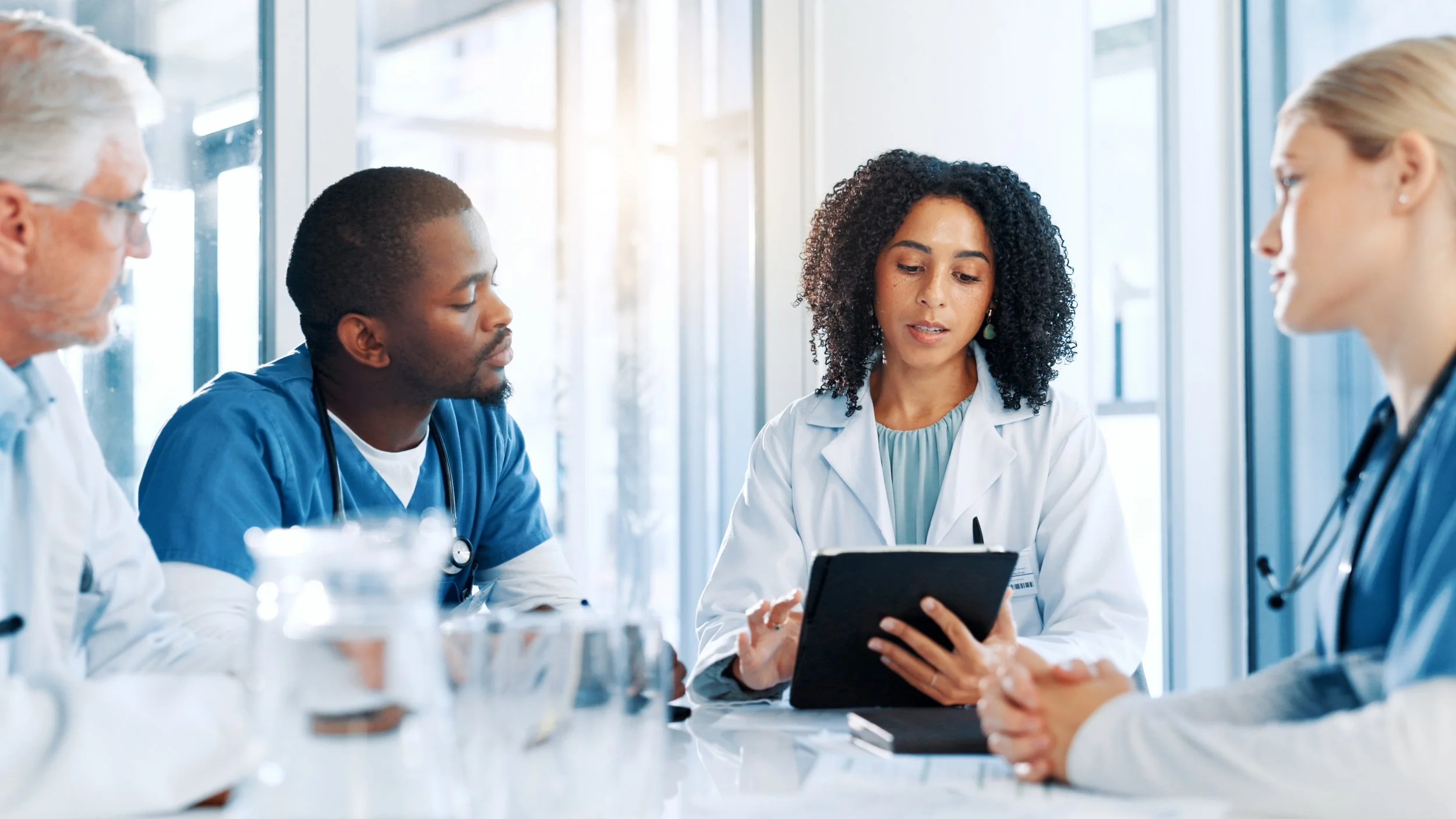 Group of healthcare professionals, including doctors and nurses, having a discussion at a conference table in a bright, modern medical facility.