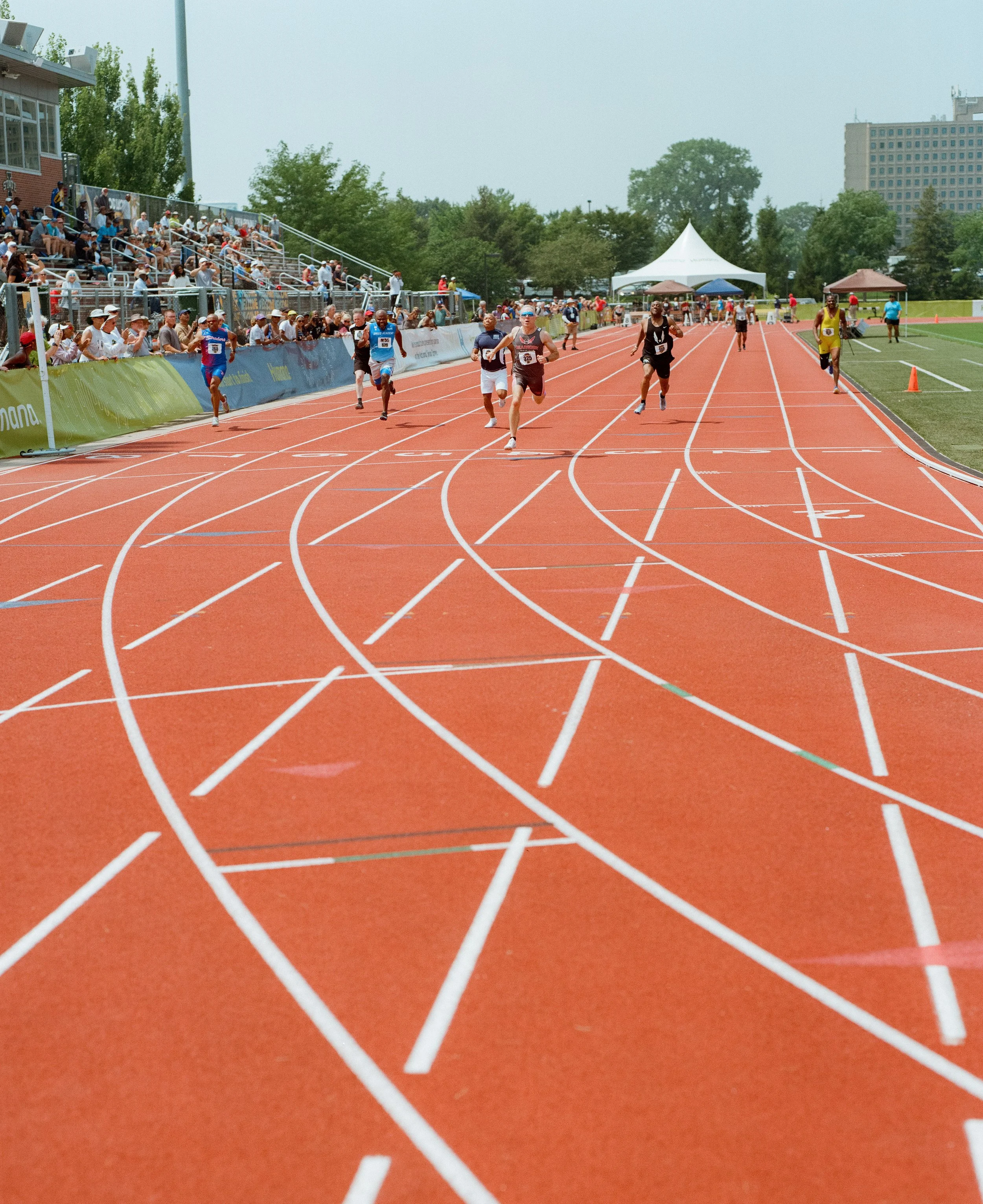 Track race with runners competing on an outdoor red running track during a sunny day.