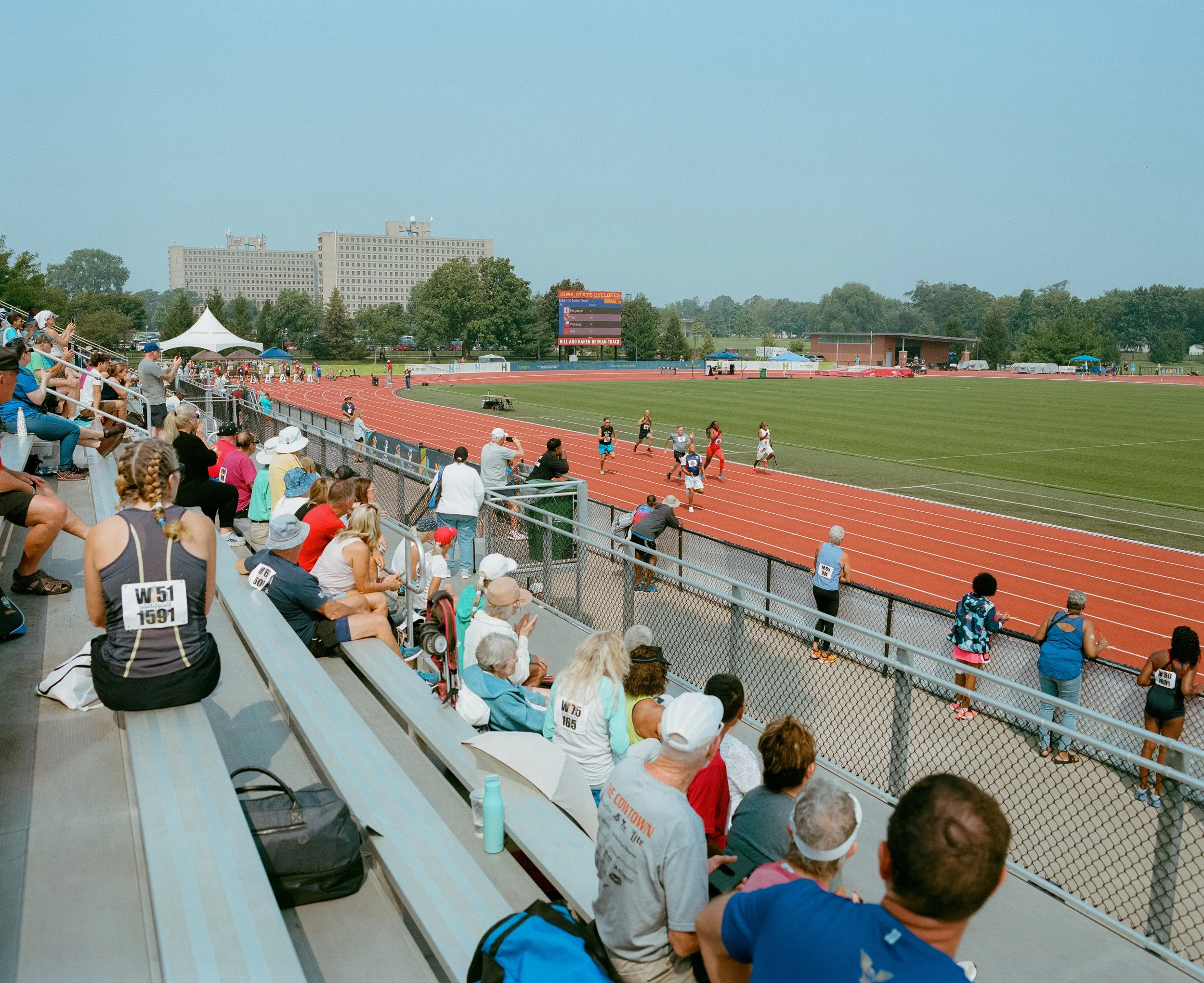 Track and field race at an outdoor stadium with spectators in bleachers and runners competing on the track.