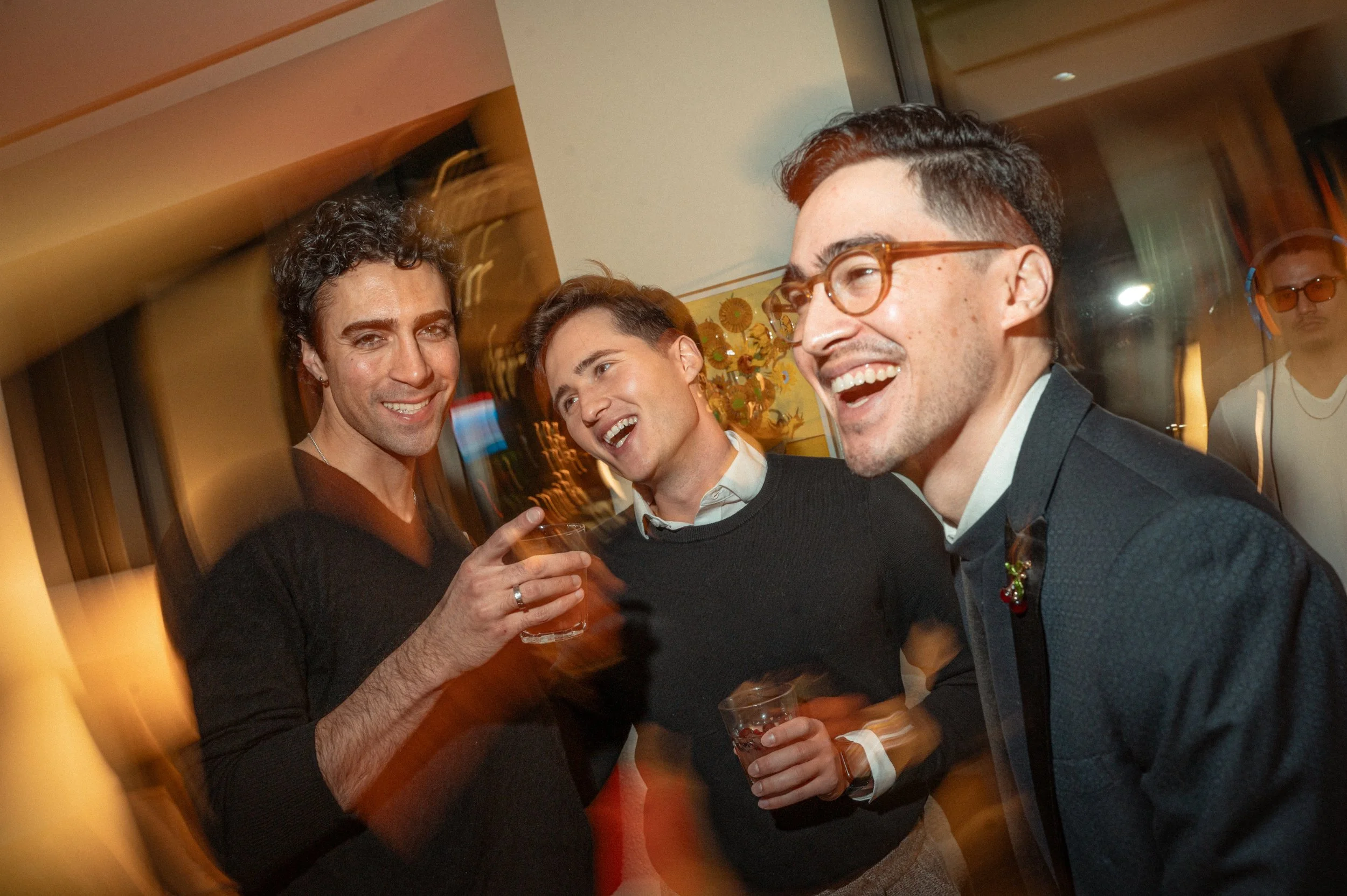 Mickey White, Rodd Cyrus, and Troy Iwata at Christmas social gathering, smiling and holding drinks. The photo has a motion blur effect.
