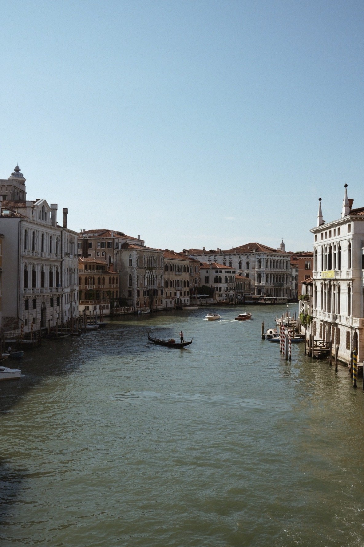 Venetian canal with boats and historic buildings on both sides under a clear blue sky.