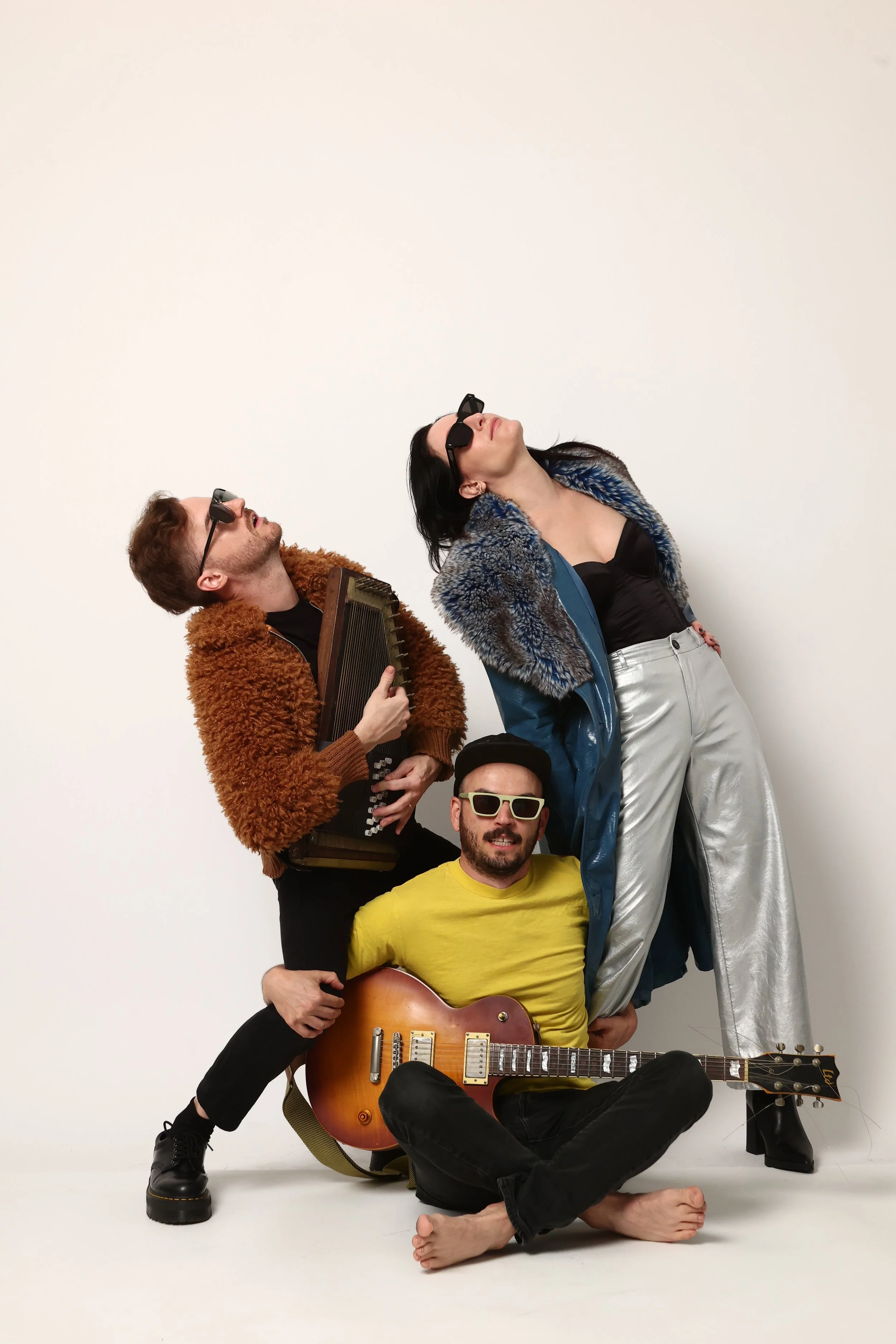 Group of people posing against a plain white background. Some are holding musical instruments and the individuals have varied hair colors and facial hair, creating a diverse and fashionable vibe.