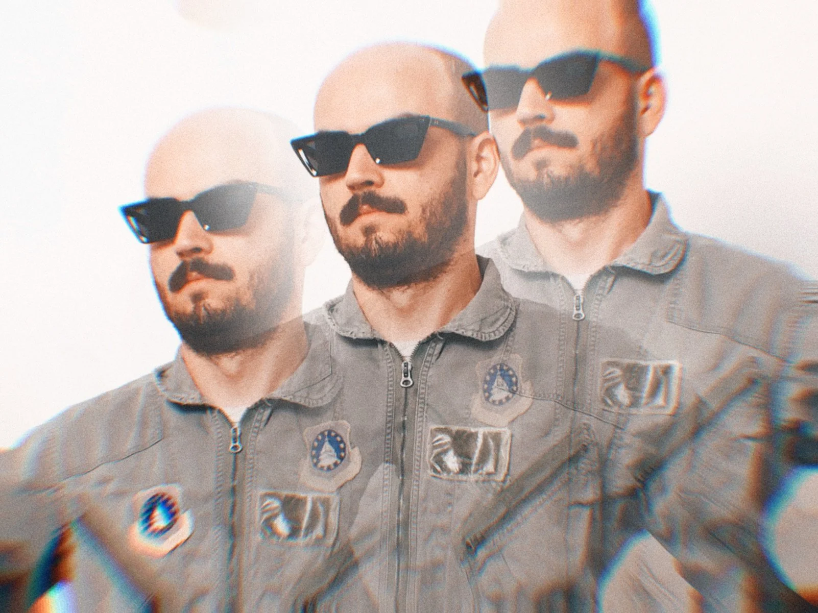 One man with a beard and sunglasses in an astronaut jumpsuit standing close together against a plain white background.