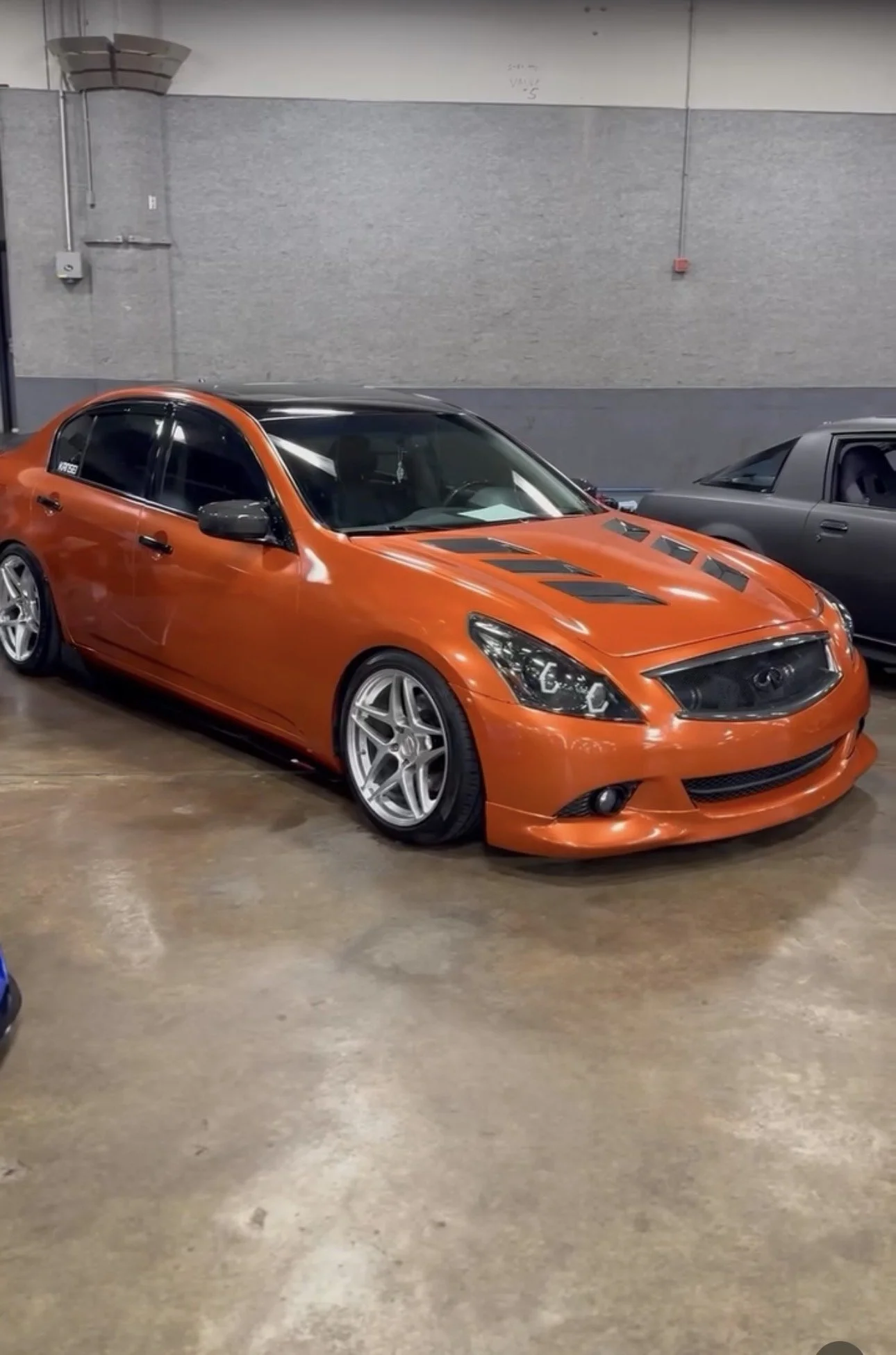 Orange custom modified Infiniti sedan with lowered suspension, black accents, and aftermarket wheels parked indoors.