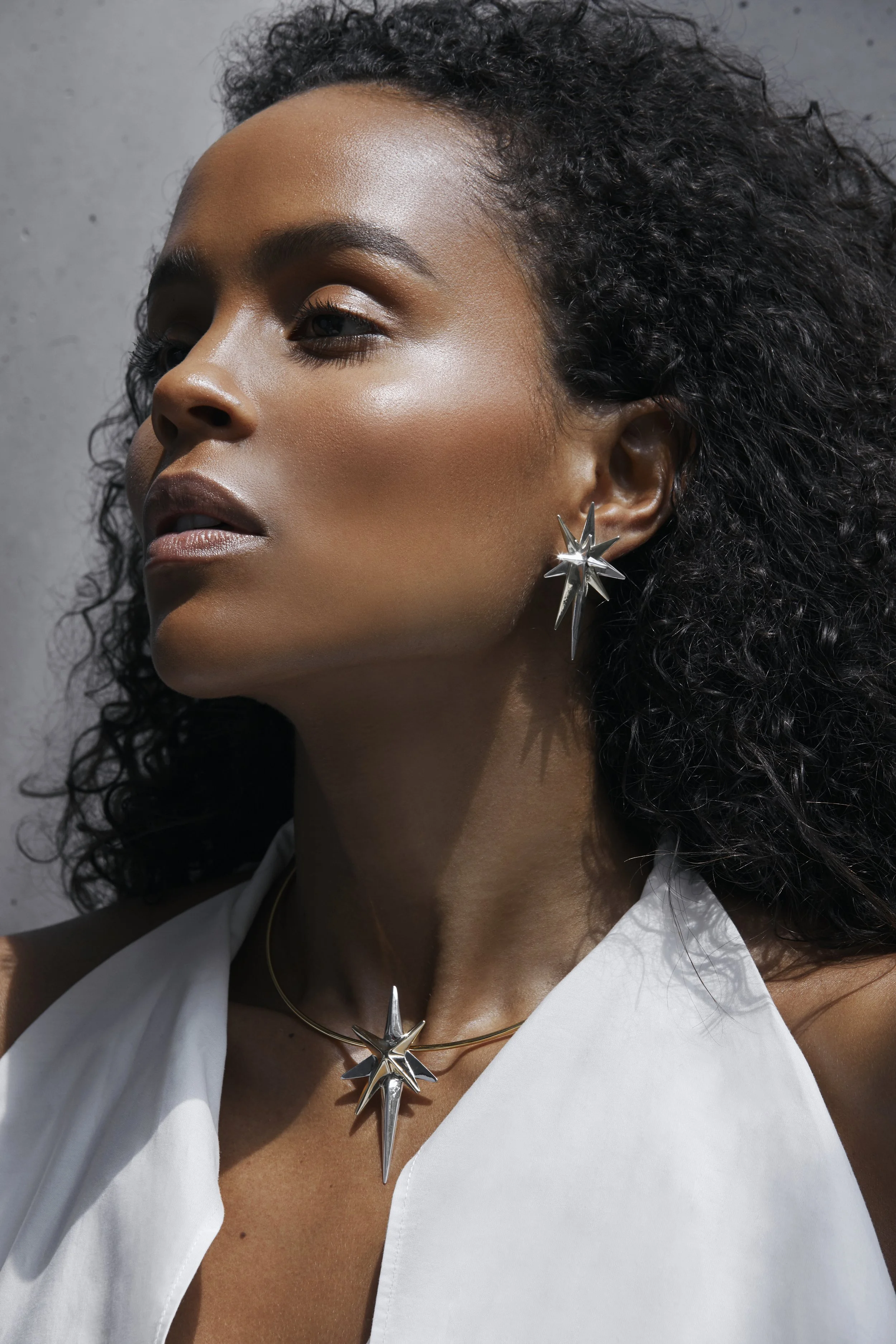 A woman with dark curly hair wearing silver star-shaped earrings and a matching star-shaped necklace.