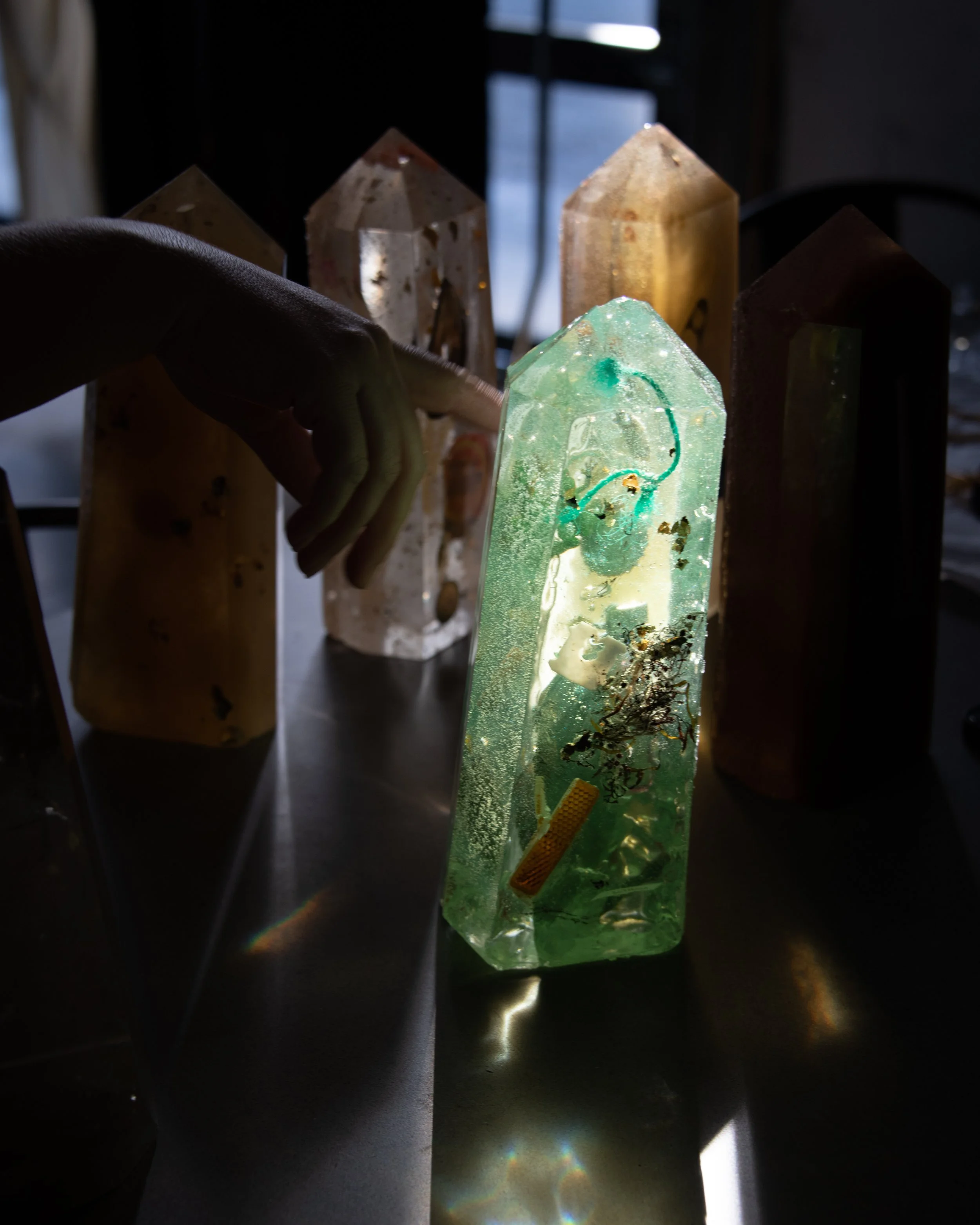 A person touching a glowing, green, translucent crystal with internal inclusions, among similar crystals on a dark surface.