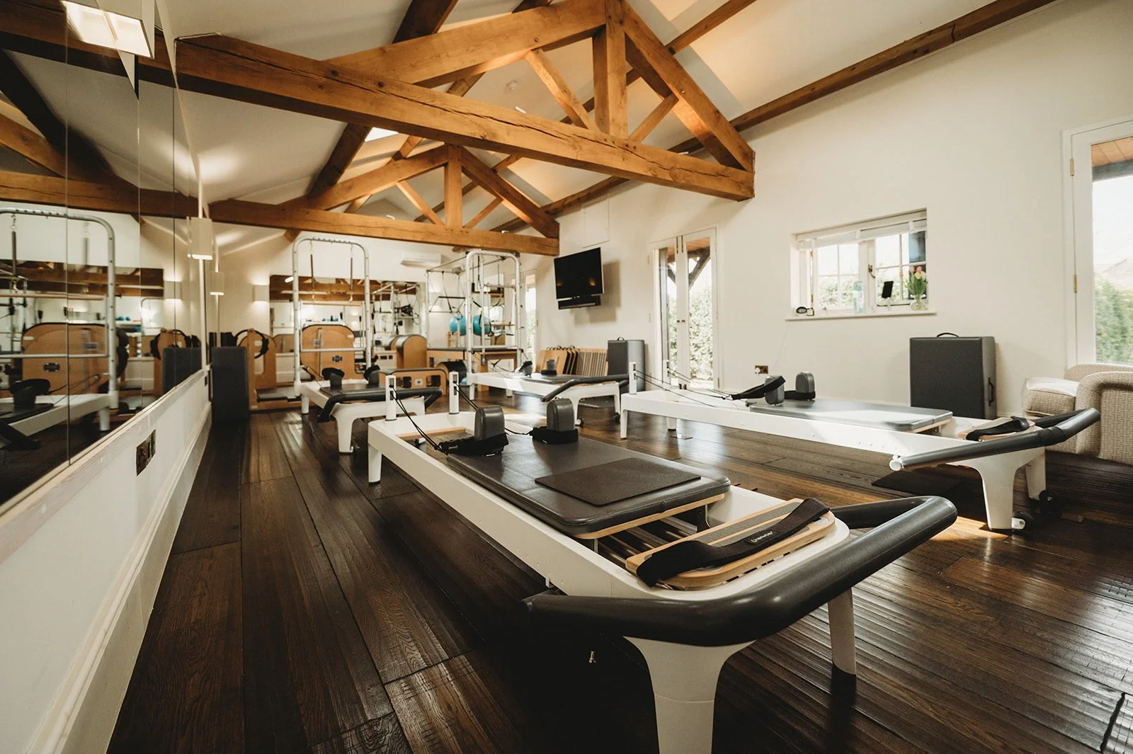 Reformer pilates studio in renovated barn with exposed beams, large mirrors and windows, and all different types of equipment, including reformers, Cadillac, Wunda chair, spine corrector, Avalon chairs and ladder barrels