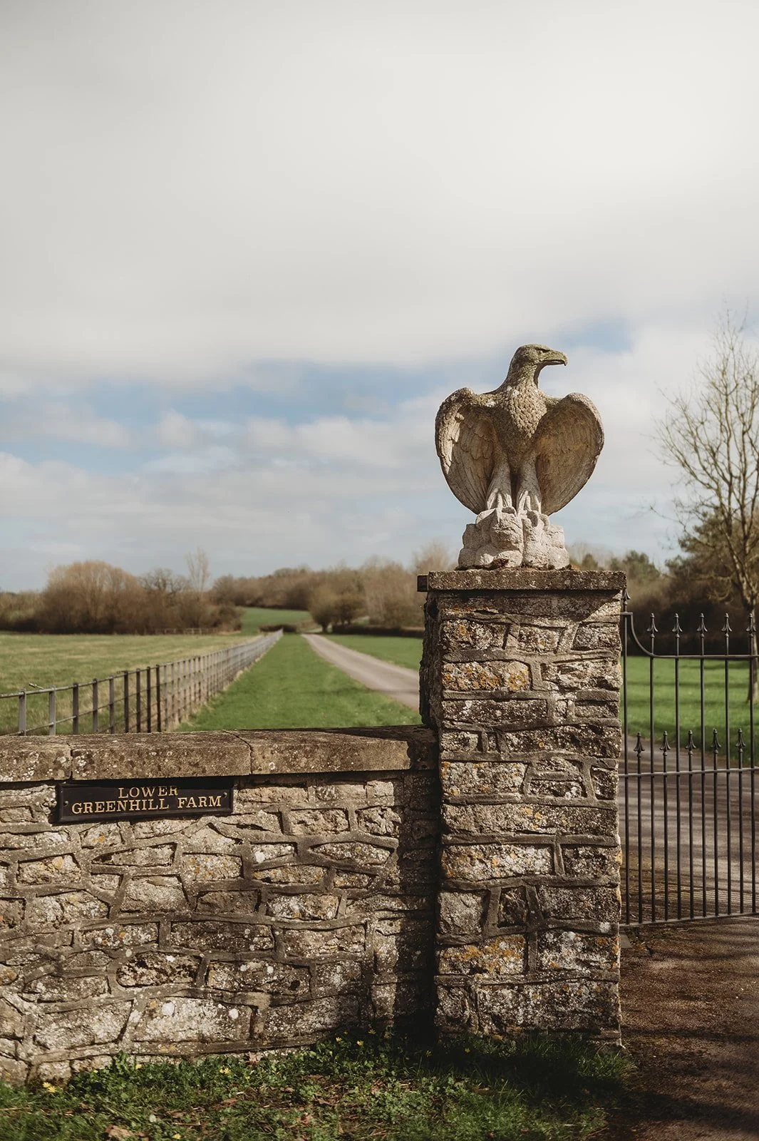 Stone eagle sitting on a stone wall with the green English countryside behind