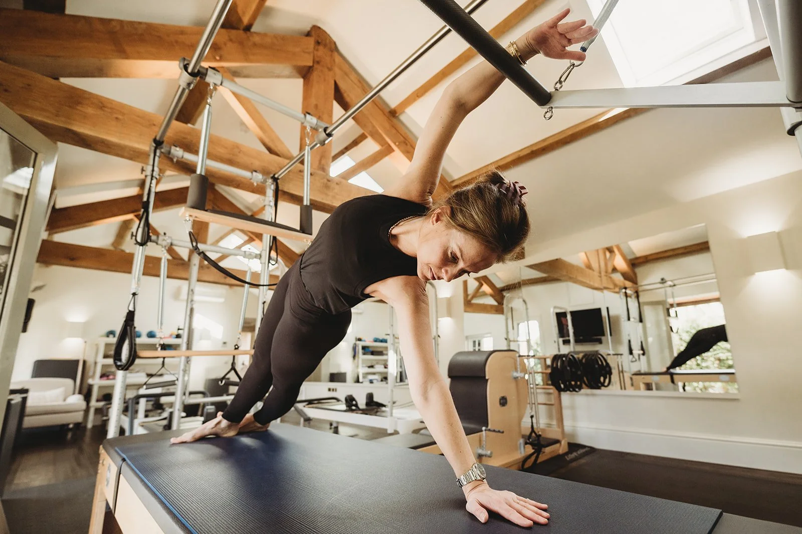 Pilates teacher holds a twisted plank pose on reformer with one hand over her head