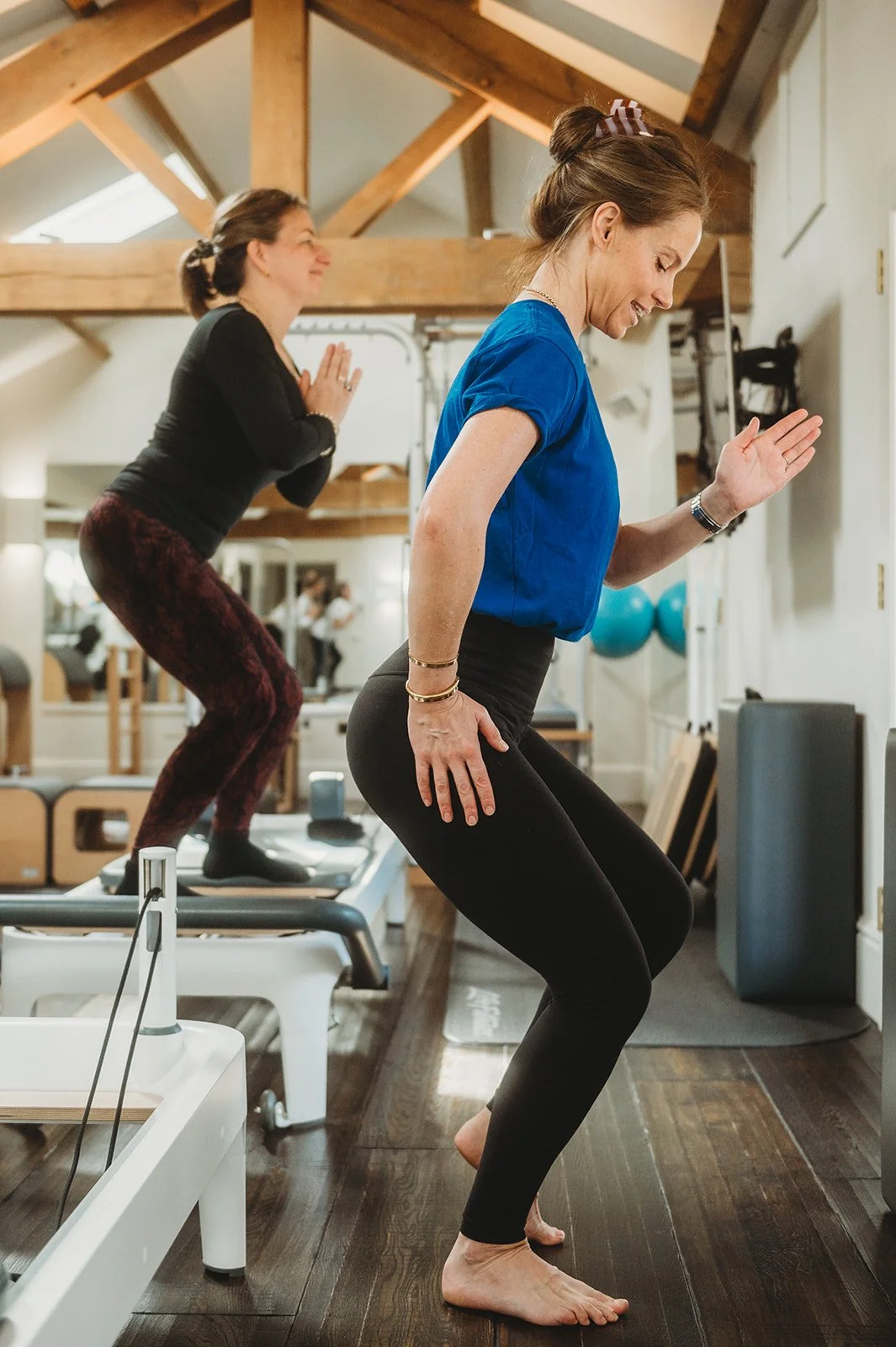 The reformer pilates teacher stands in front of the class while the students behind stand on top of their reformers