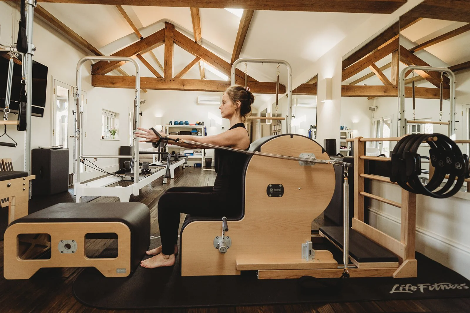 Pilates teacher demonstrates how to use the F2 Arm Chair by BASI Systems by sitting down and putting forward on the cords with her arms