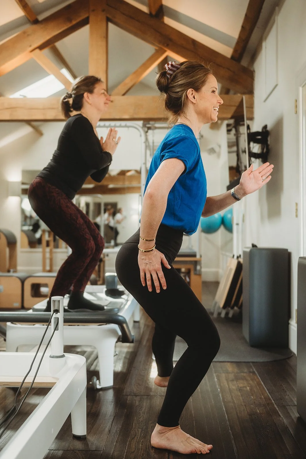 Female pilates teacher smiles while showing how to do the exercise in front of the small class of reformer pilates