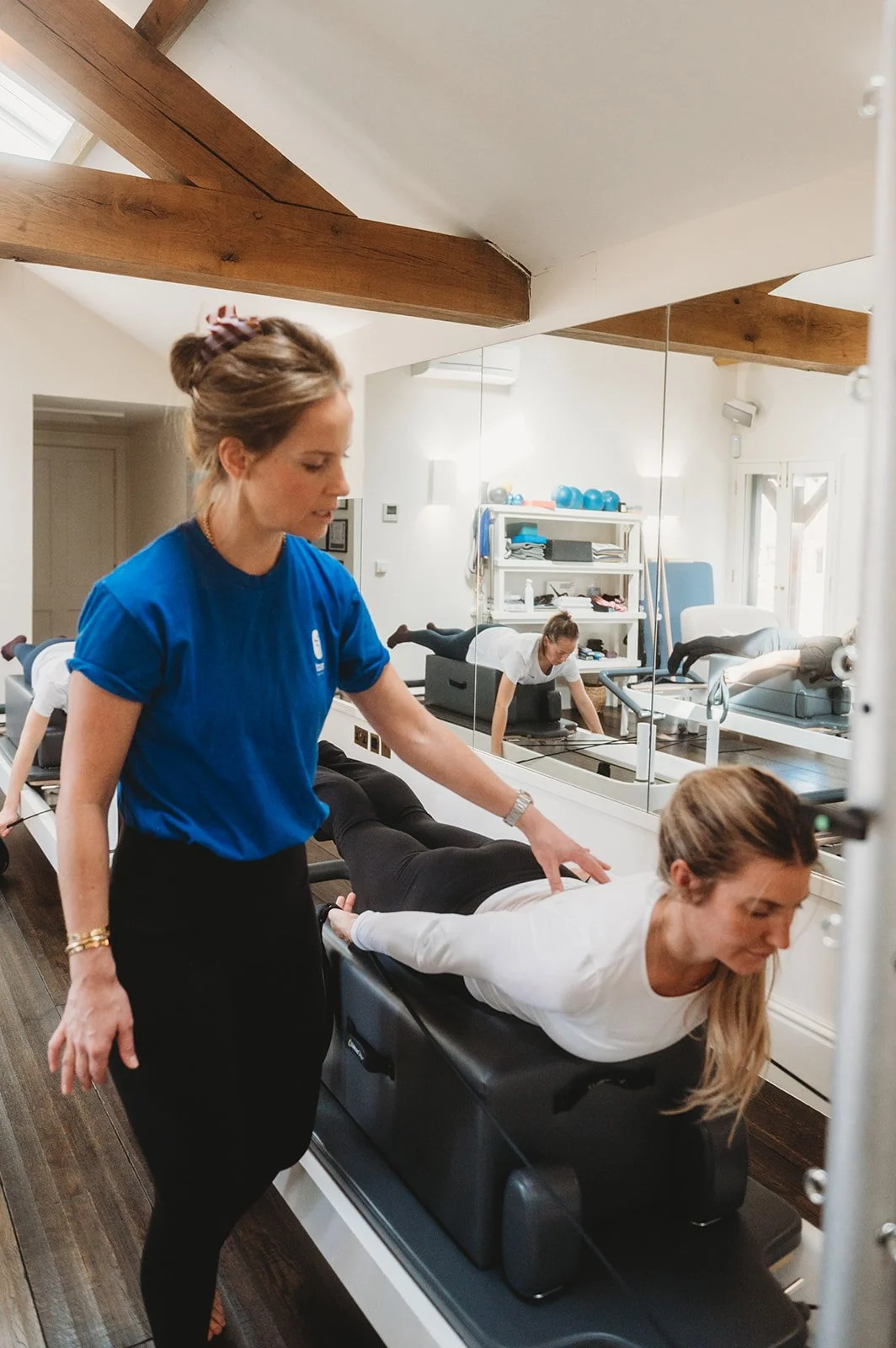 Female pilates teacher gently touching the back of a female student while the student works out on a reformer