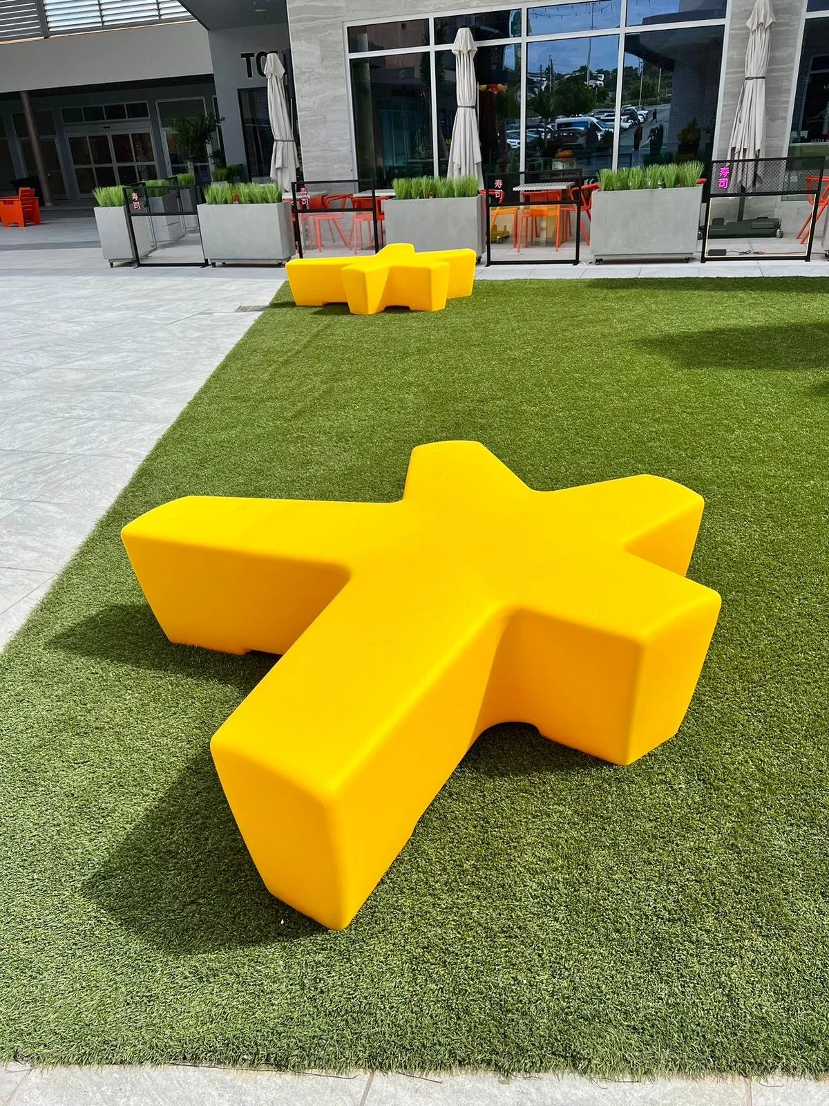 Yellow star-shaped outdoor seating sculpture on artificial grass outside a modern building.