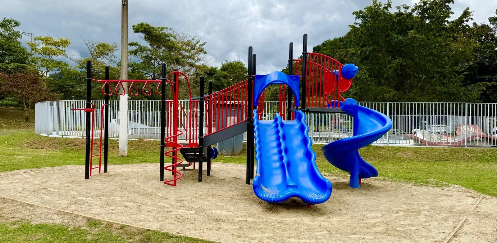 Colorful playground with slides, climbing structures, and a spiral slide, surrounded by grass and trees.