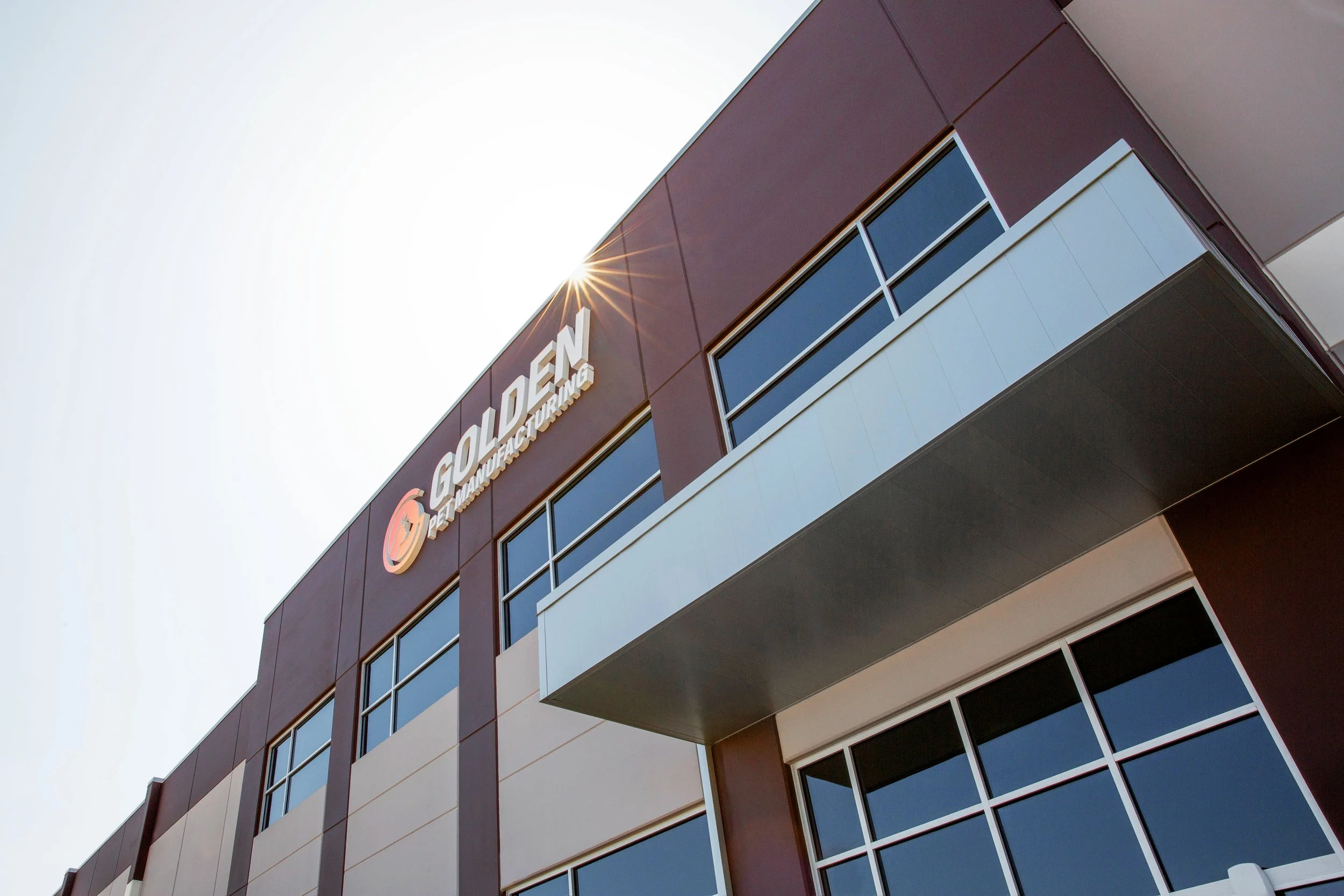 Exterior of a modern building with a sign that reads GOLDE Bond Manufacturing, with the sun shining behind it.