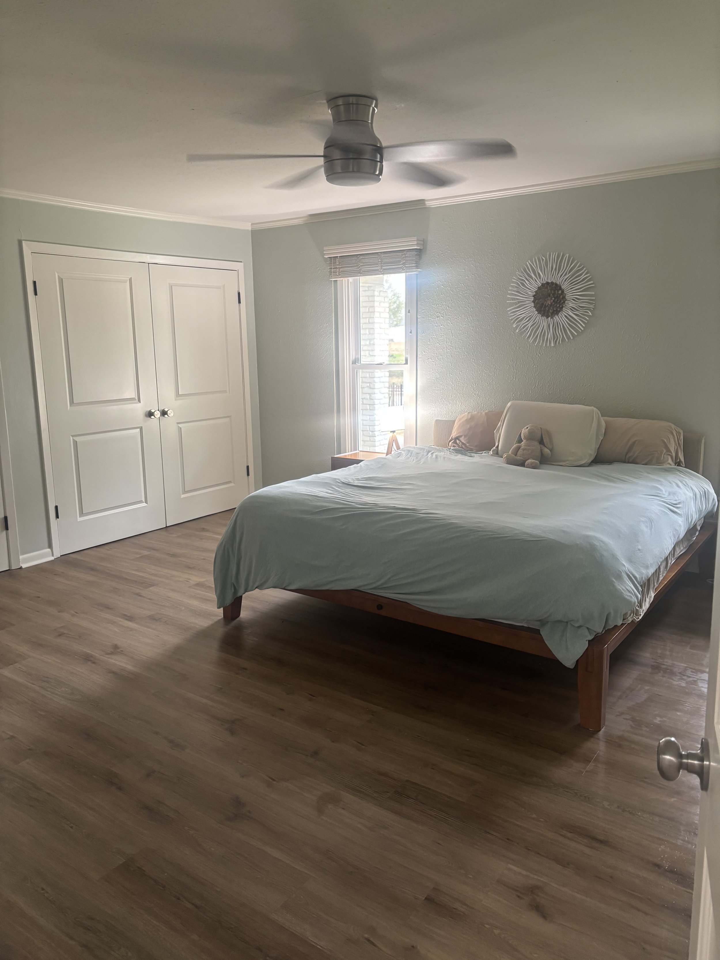A bedroom with a bed, a ceiling fan, a window, a closet, and a wall-mounted decorative piece.