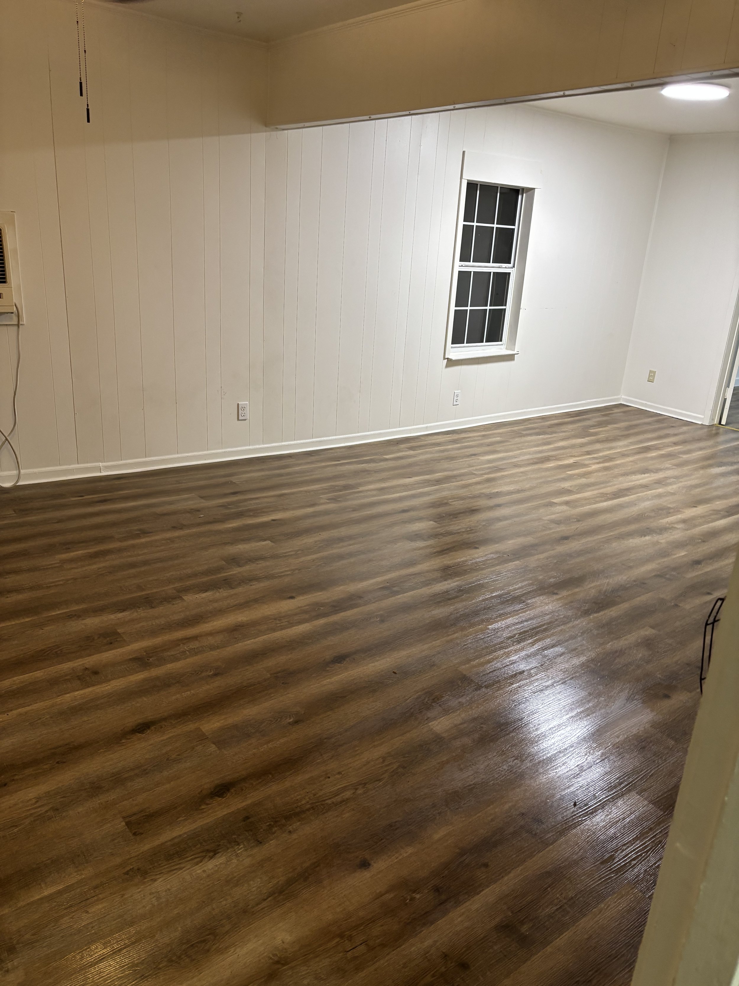 Empty room with hardwood floors, white paneled walls, a window with gridpanes, and ceiling lights.
