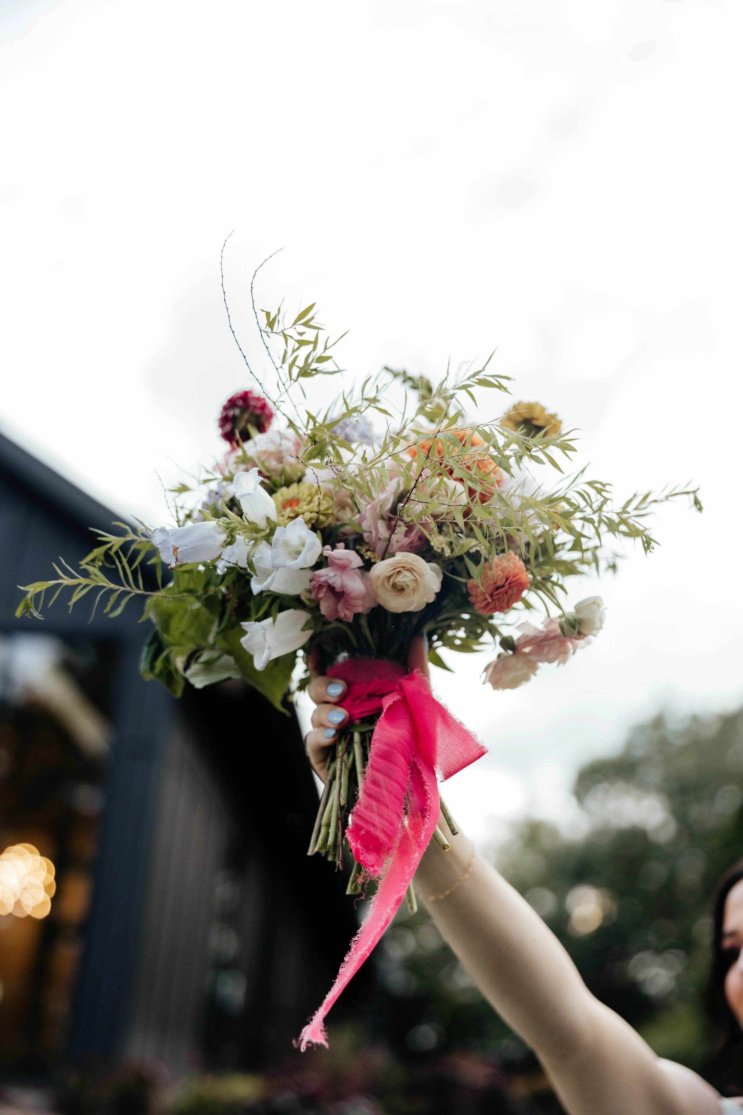 A person holding a colorful bouquet of flowers decorated with a bright pink ribbon