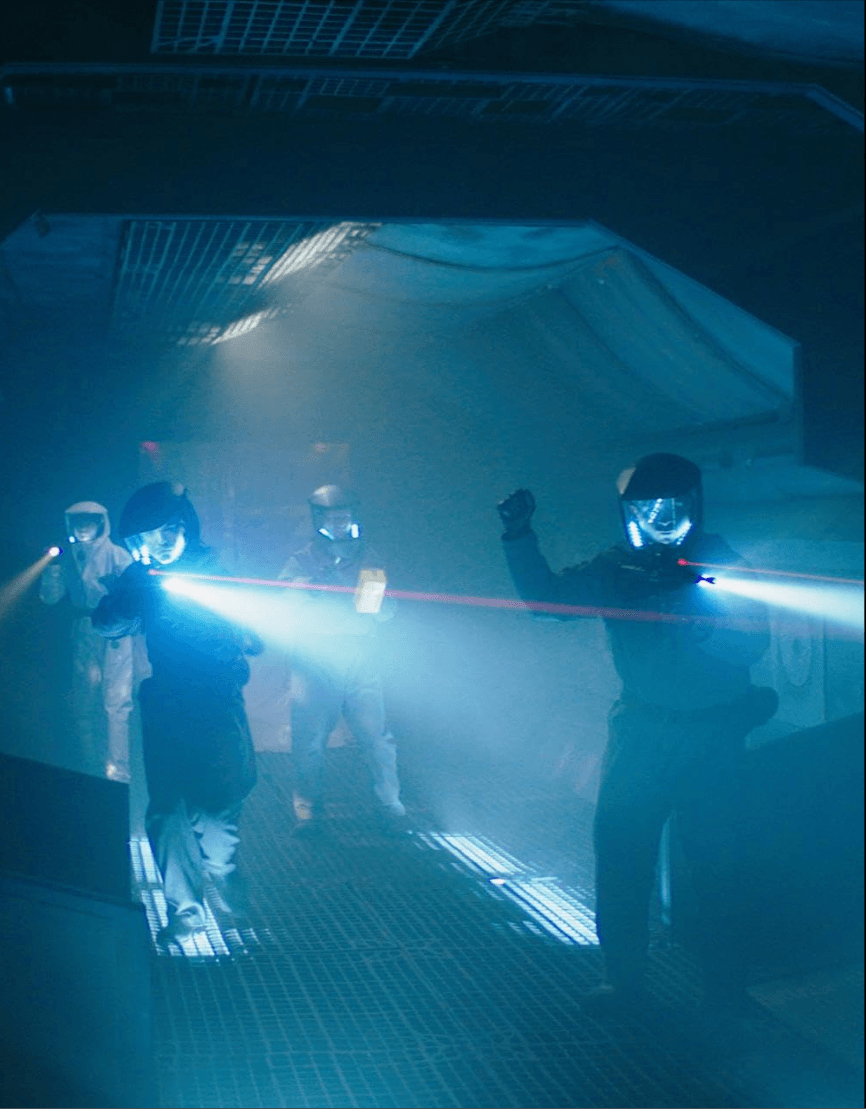 People wearing protective suits and helmets using laser equipment in a dark, foggy environment.