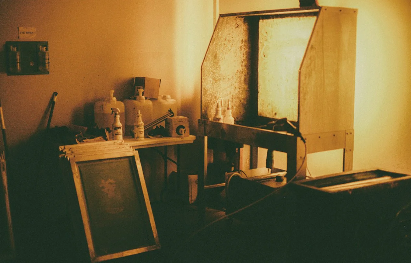 A dimly lit room with vintage cleaning equipment, including bottles, a screen, and a wooden machine, suggesting it is an old photo developing or printing setup.