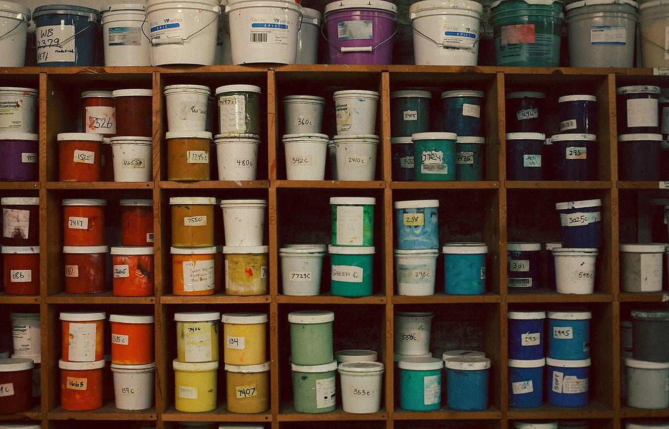 Shelves filled with rows of paint buckets in various colors, labeled with handwritten tags.