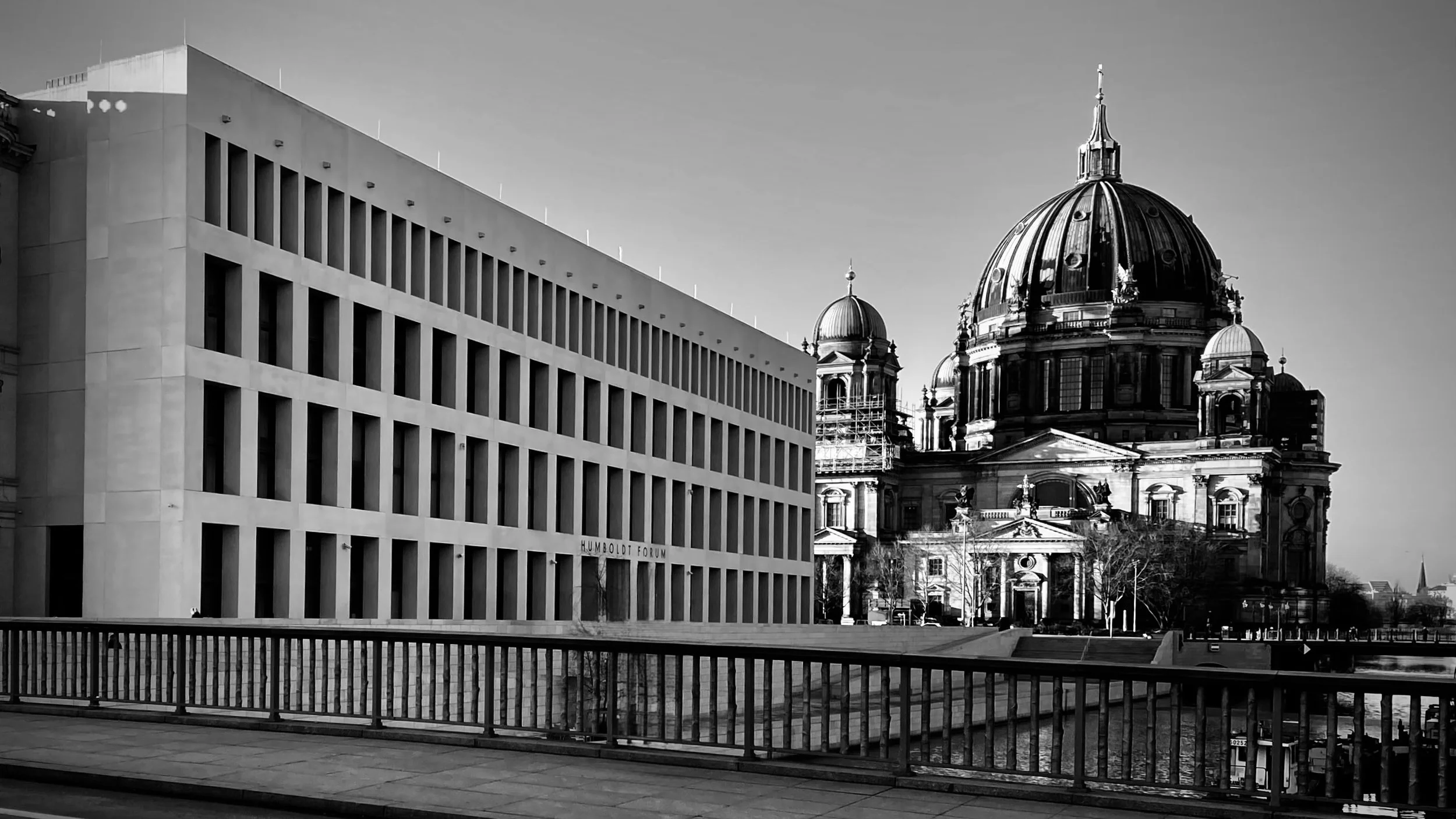 Schwarz-weiß-Foto von einer modernen Bürogebäude und einer barocken Kirche im Hintergrund, mit Wasser im Vordergrund und Brüstung im Vordergrund.