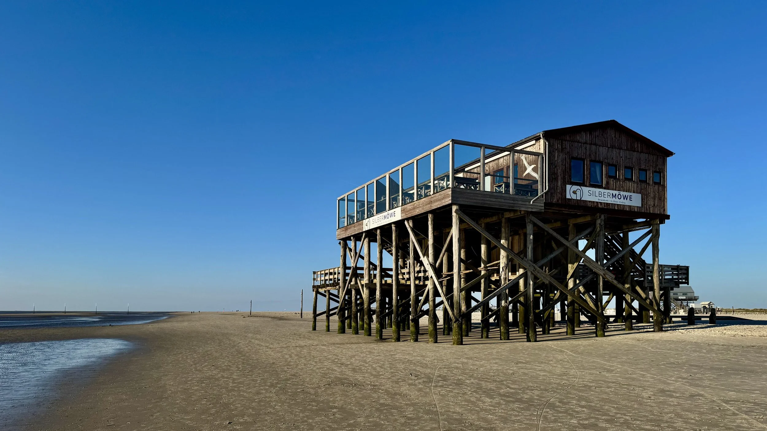 Ein Holzbau auf Stelzen am Strand mit klarem blauen Himmel im Hintergrund.
