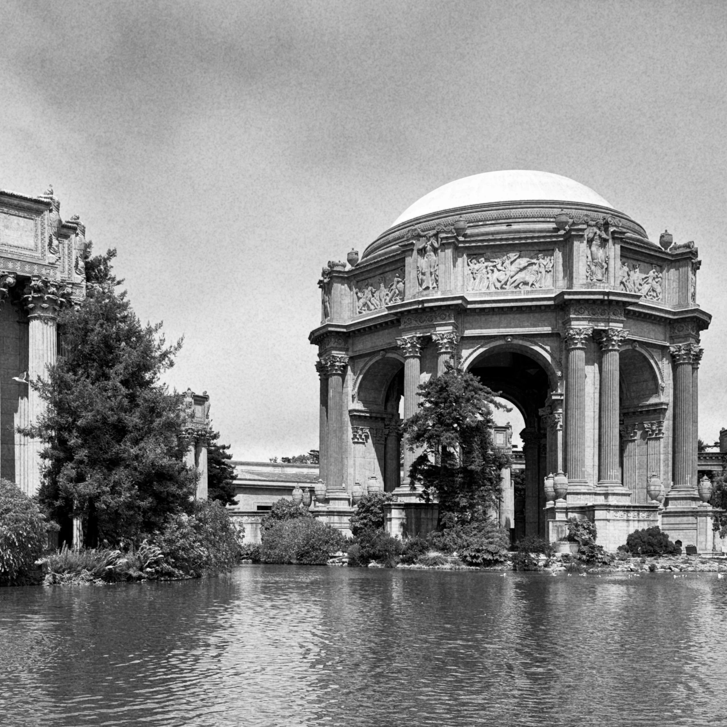 Eine historische römische Architektur mit einer großen Kuppel, Säulen und Reliefs, umgeben von Wasser und Bäumen.