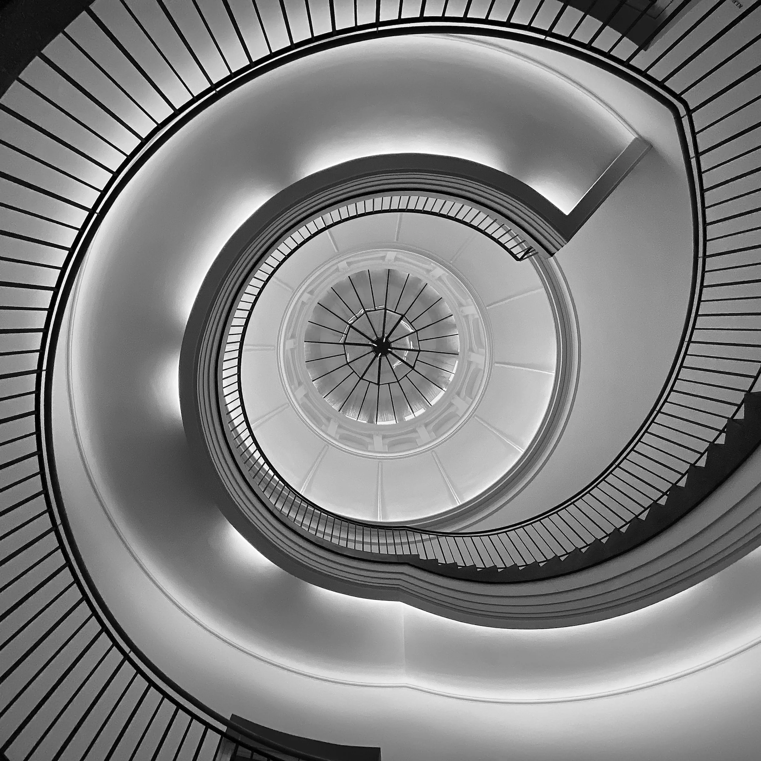 Innenansicht einer spiralförmigen Treppe in schwarz-weiß, die nach oben führt, mit Glaskuppel im oberen Bereich
