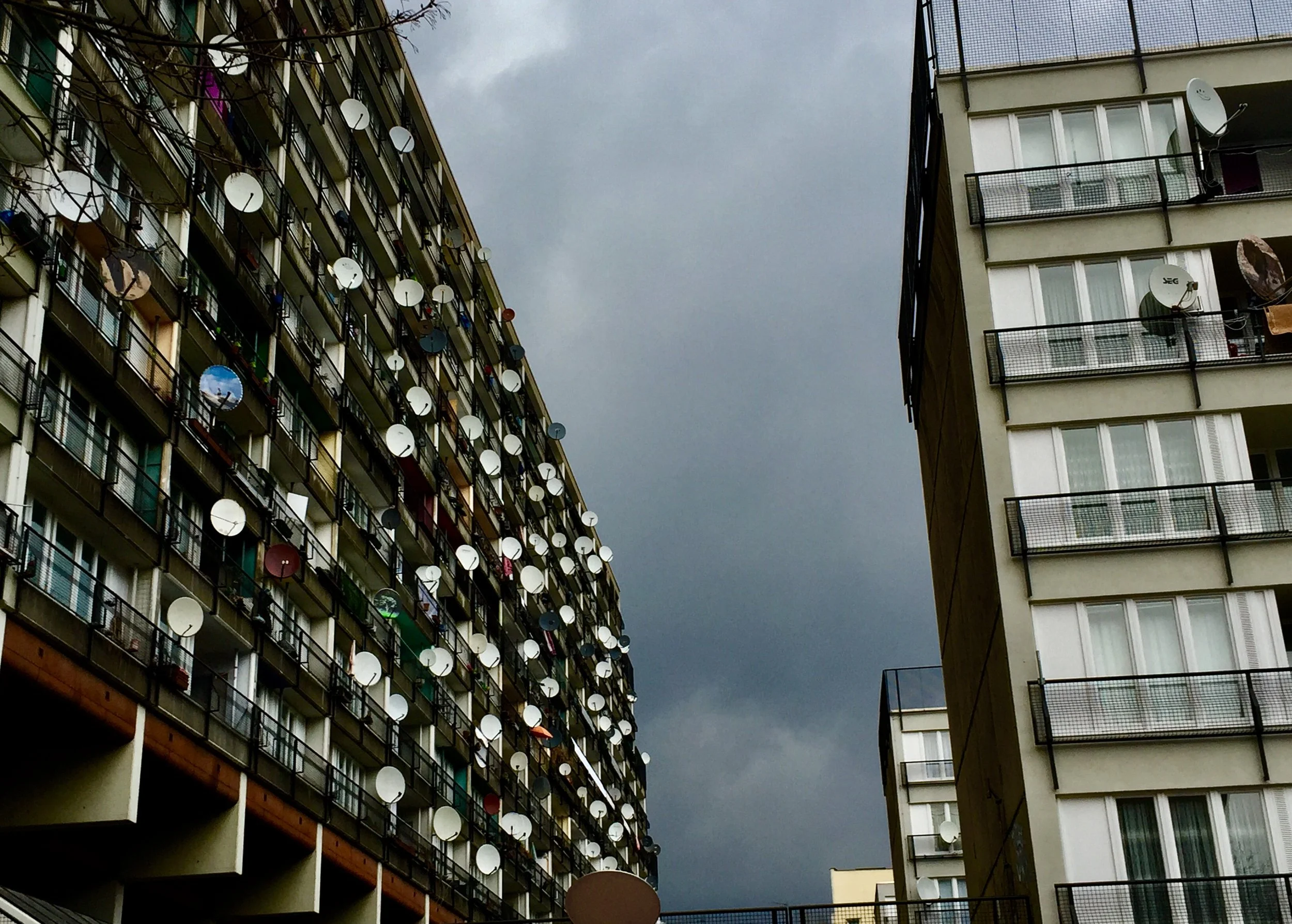 Mehrere Hochhäuser mit zahlreichen Satellitenschüsseln an den Balkonen, dunkler Himmel mit Wolken im Hintergrund.
