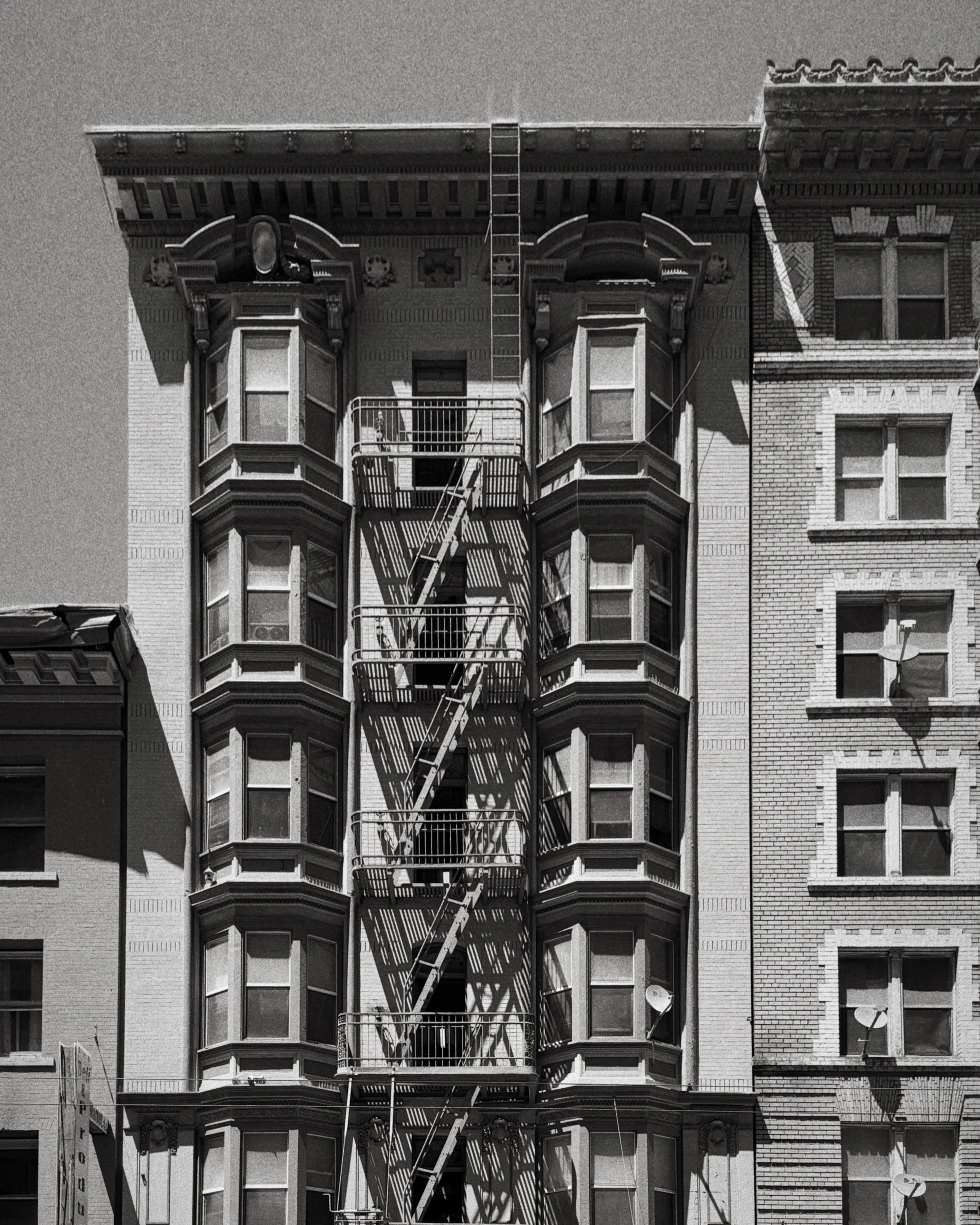 Schwarze und weiße Aufnahme eines alten mehrstöckigen Gebäudes mit Feuerleitern, Fenstern und einem gezackten Dach.
