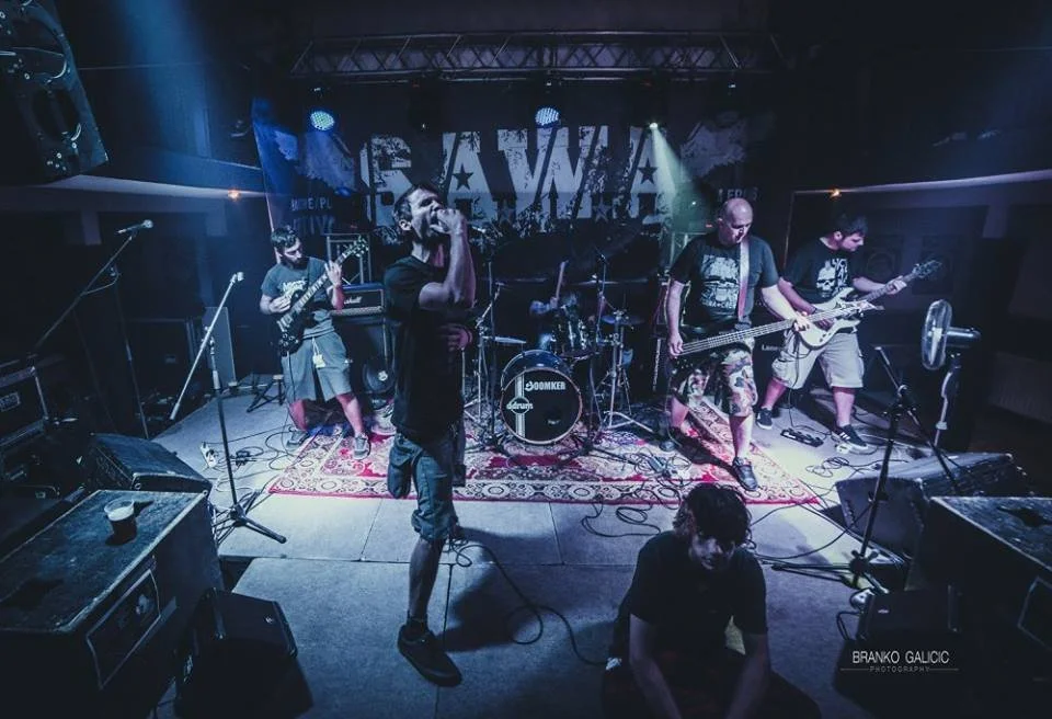 A band performs live on stage with five members, including a singer, guitarists, bass player, and drummer, in a dark club setting with blue stage lights.