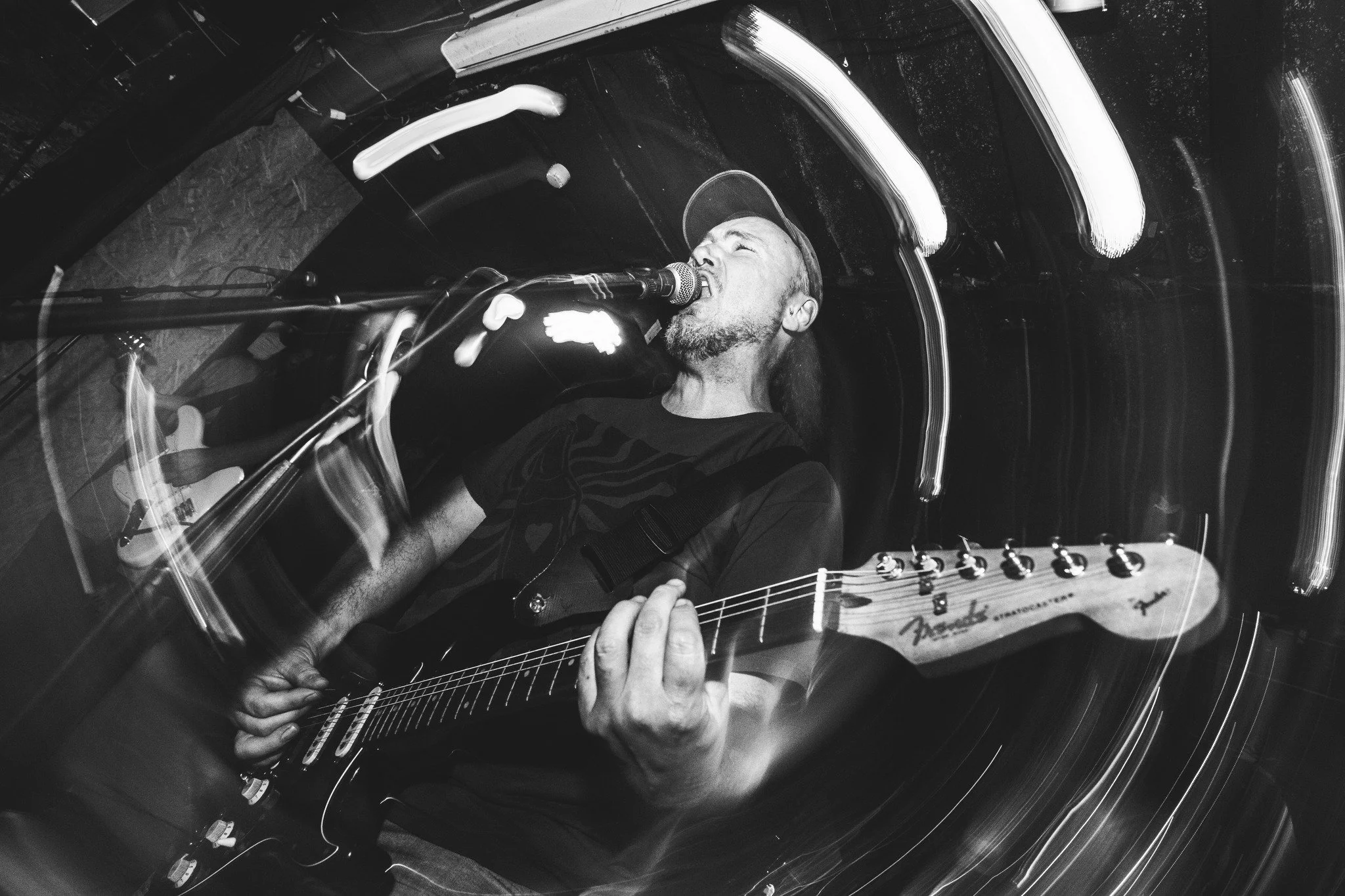 A person playing an electric guitar, singing into a microphone, photographed in black and white with motion blur effects.