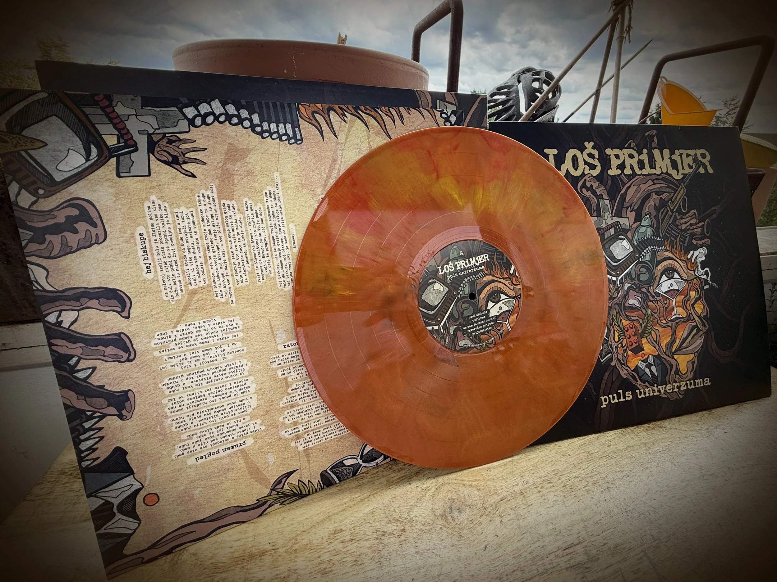 A pink and orange vinyl record leaning against a graphic album cover with illustrations of musical instruments and a lion with a music-themed design.