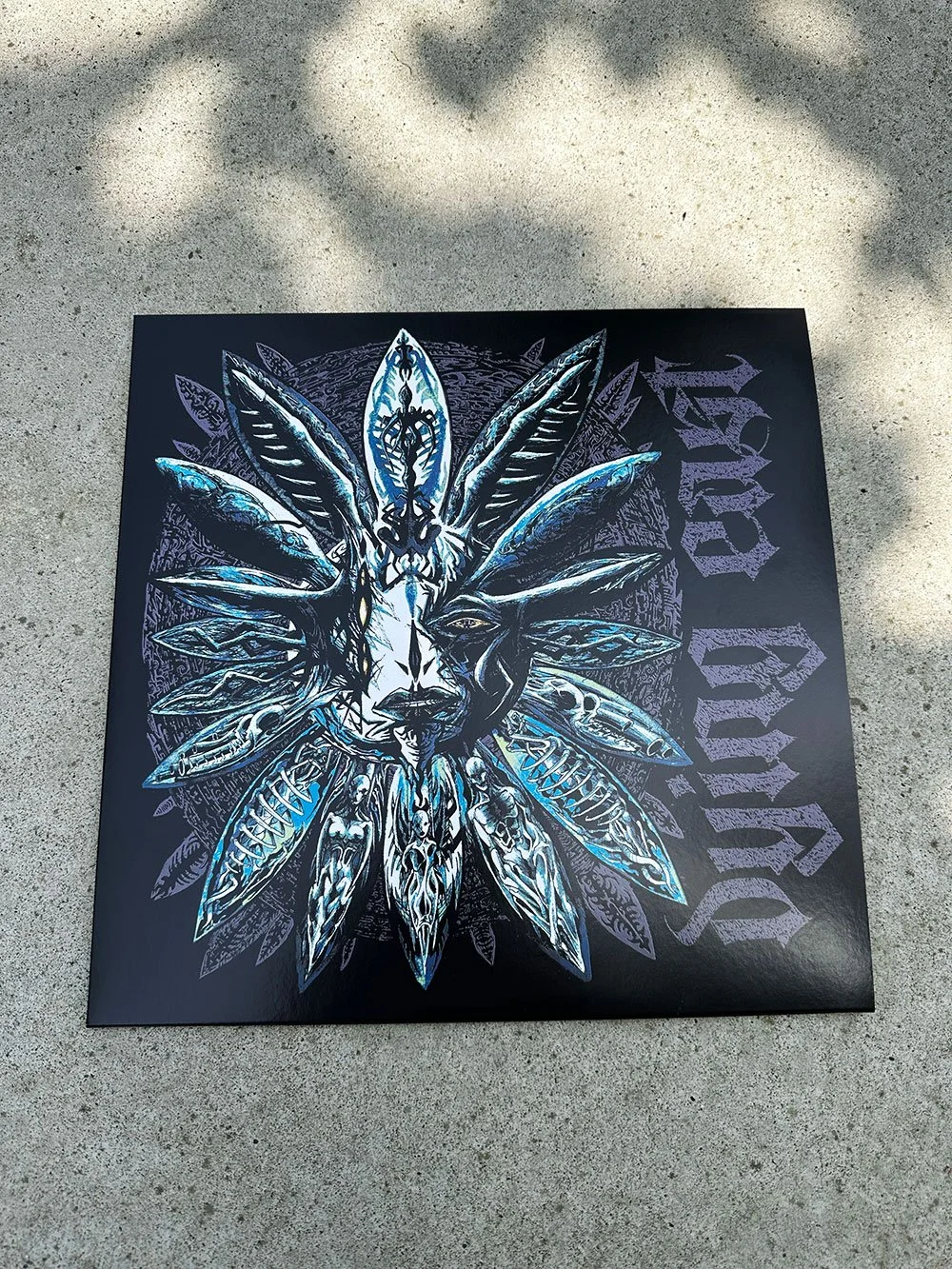 A black square canvas featuring a stylized, intricate artwork of a face surrounded by feather-like designs, with text reading 'Dying East in gothic font.