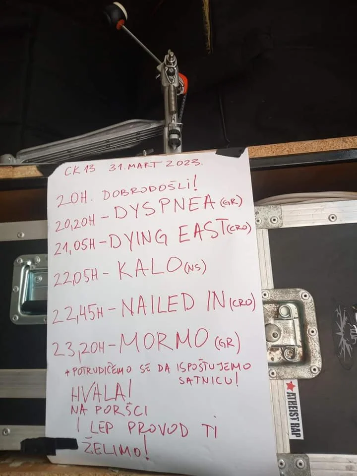 A handwritten schedule on a white sheet of paper attached to a case or equipment, listing times and activities with some notes and greetings, written in red ink.