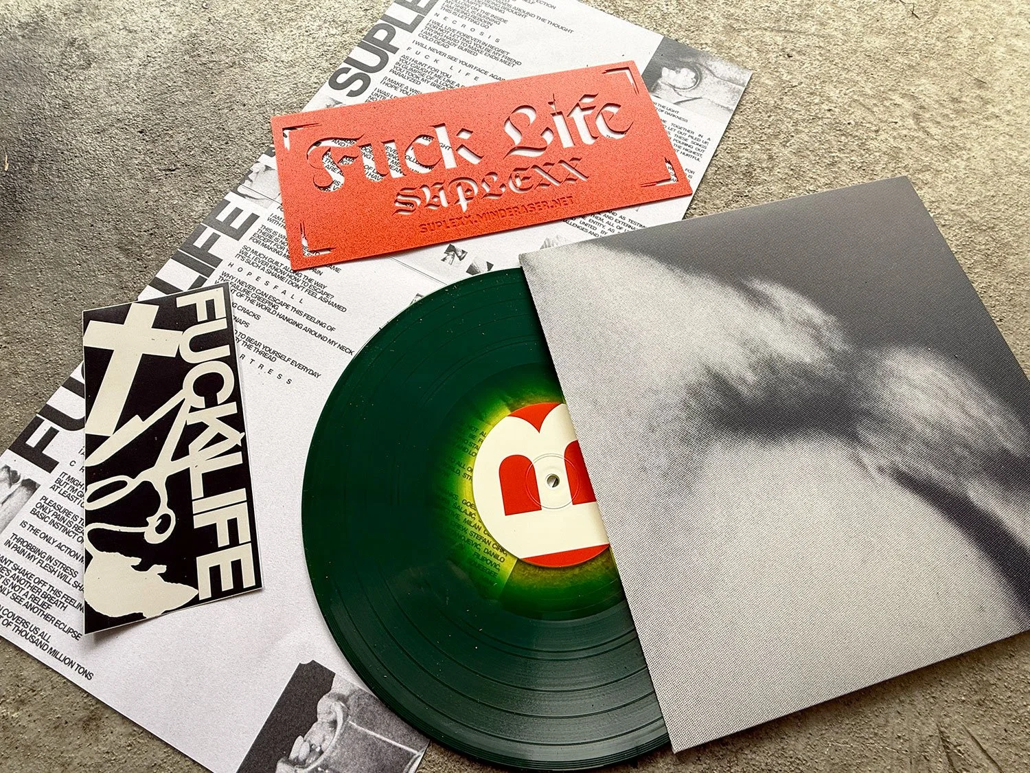 A collection of vinyl records, posters, and paper items on a concrete surface, including a black and white sticker, a red stencil, and a gray album cover with a cloud pattern.