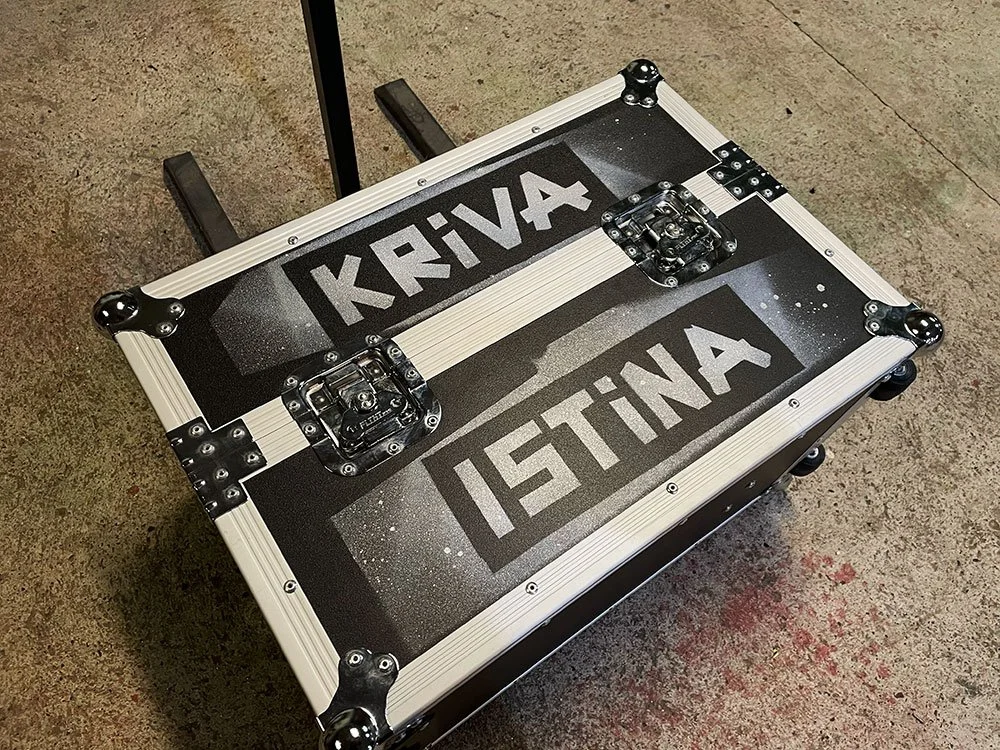 A black and silver flight case with the words 'KRIVA' and 'ISTINA' written on it, placed on a concrete floor. The case has metal hardware and corner protectors.